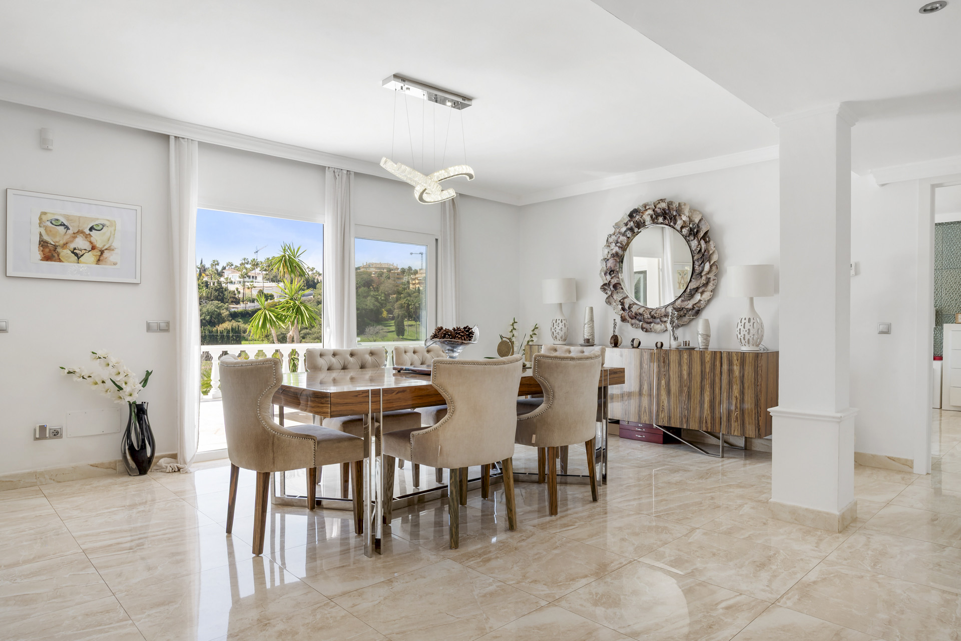 Dining room with large windows overlooking a green landscape and a modern chandelier.