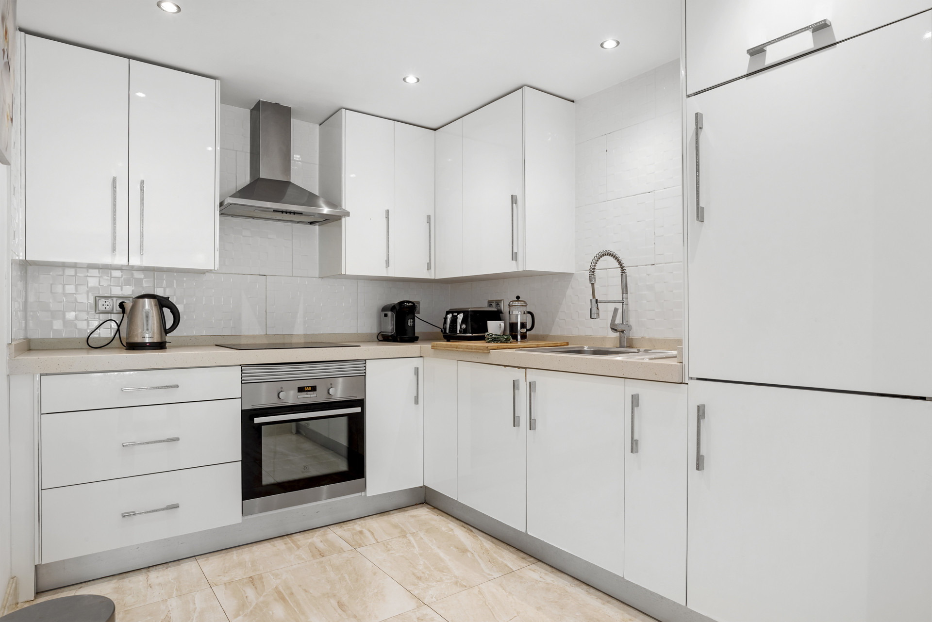 White kitchen with stainless steel appliances, a corner layout, and white tiled backsplash and cabinets.
