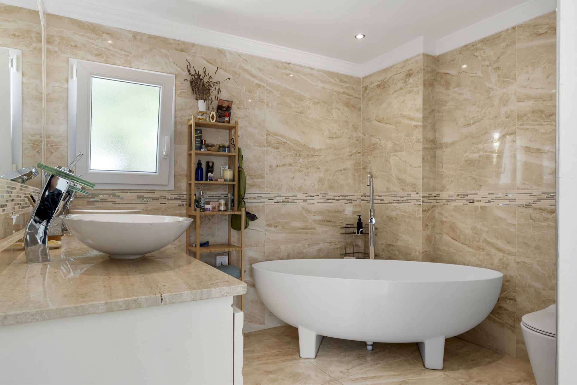 Bathroom with a freestanding soaking tub, dual vessel sinks, marble tiling, and a small frosted window.