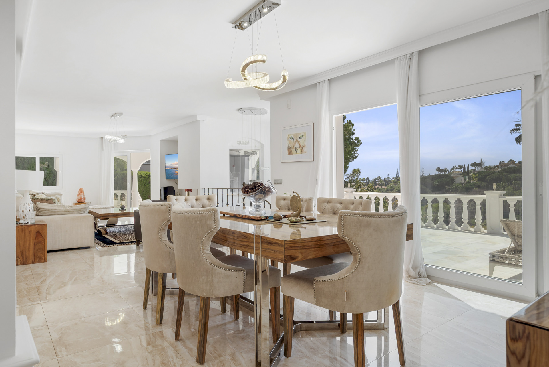 Dining area with a polished wooden table, upholstered chairs, modern chandelier, and sliding doors to a terrace.