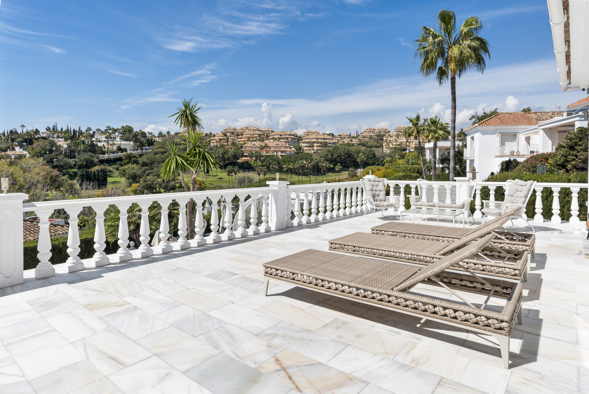 Expansive outdoor terrace with lounge chairs, white balustrades, and distant views of a town and golf course.