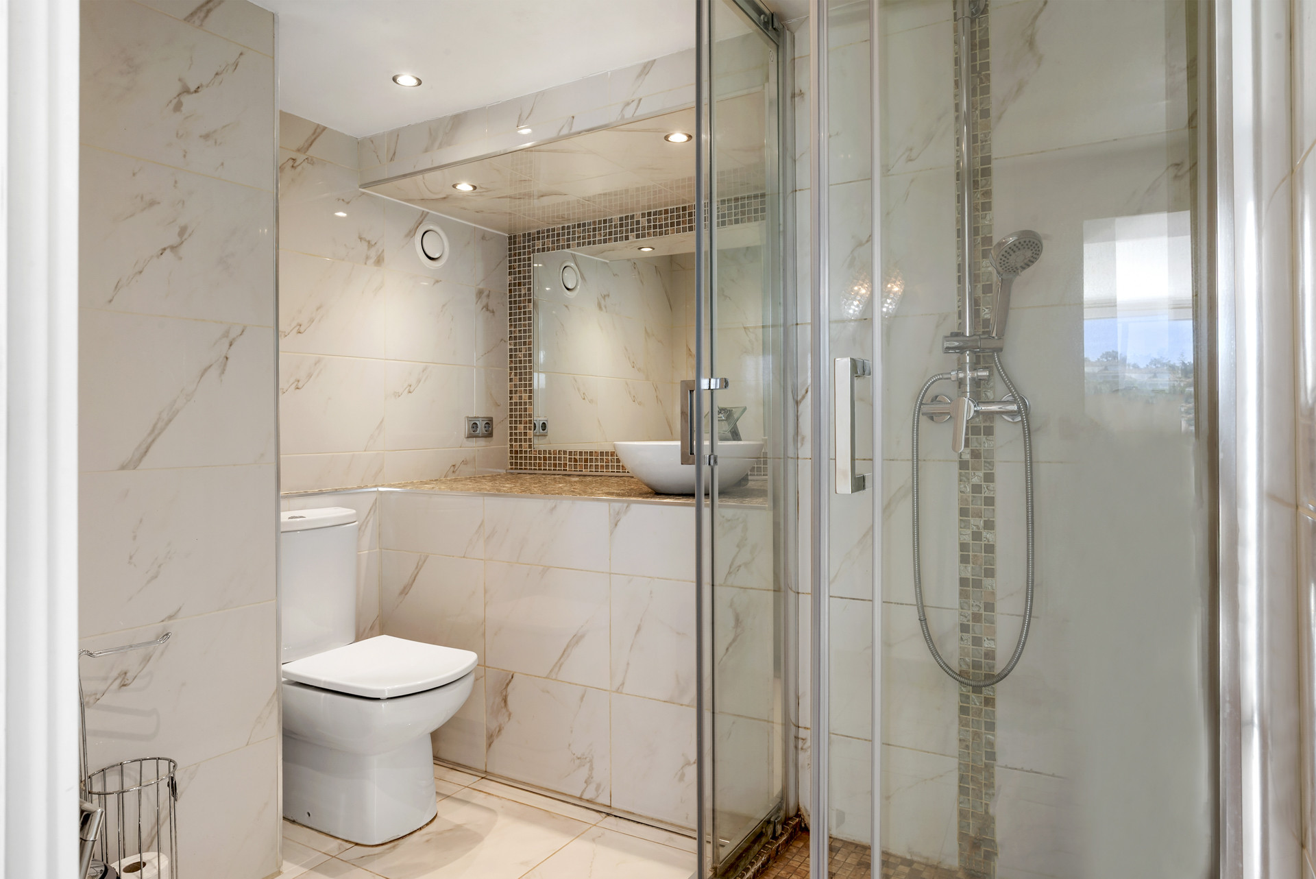 Bathroom with tiled walls, shower enclosure, toilet, and sink with mirror above.