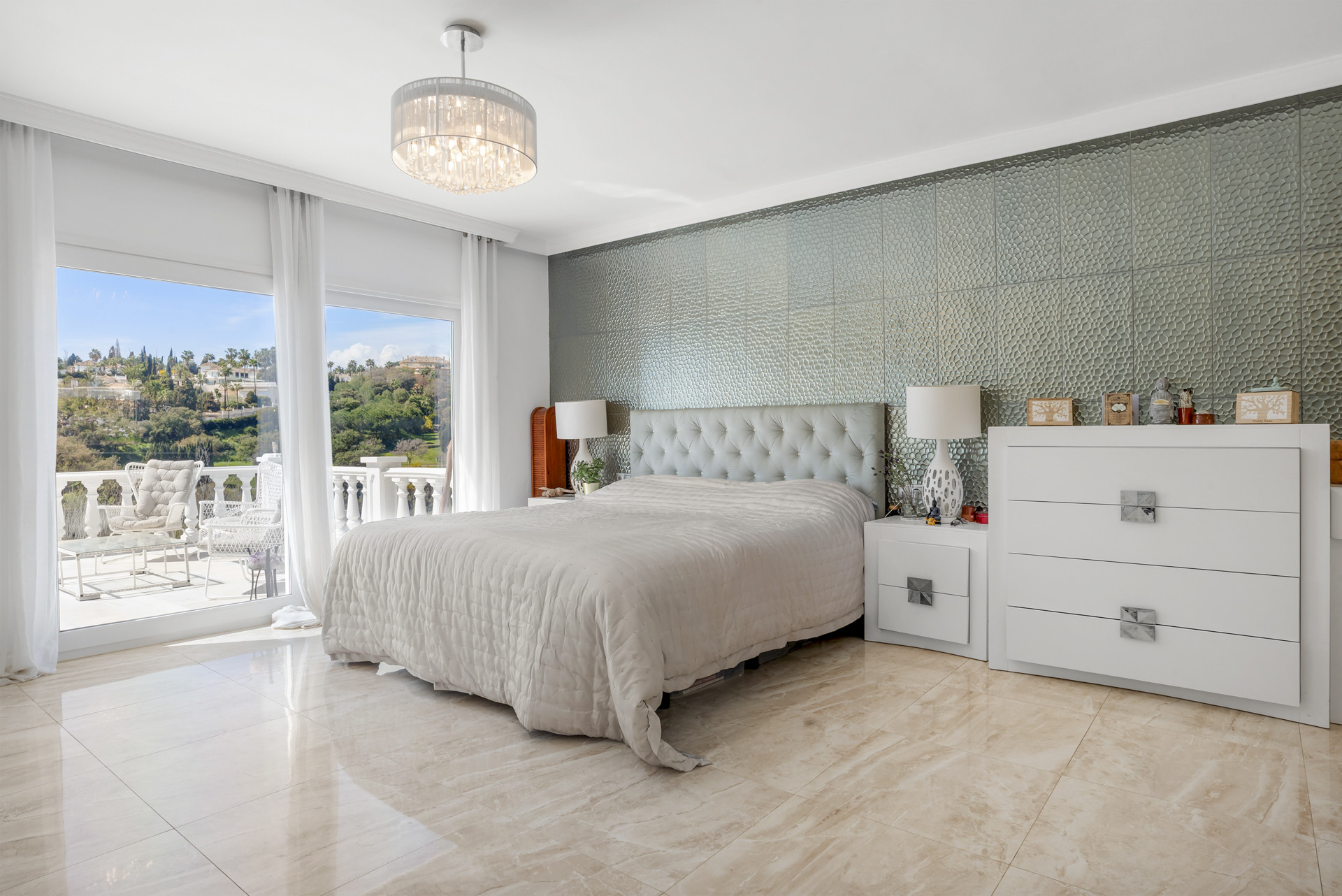 Bedroom with a large bed, textured accent wall, chandelier, and sliding glass doors opening to a balcony.
