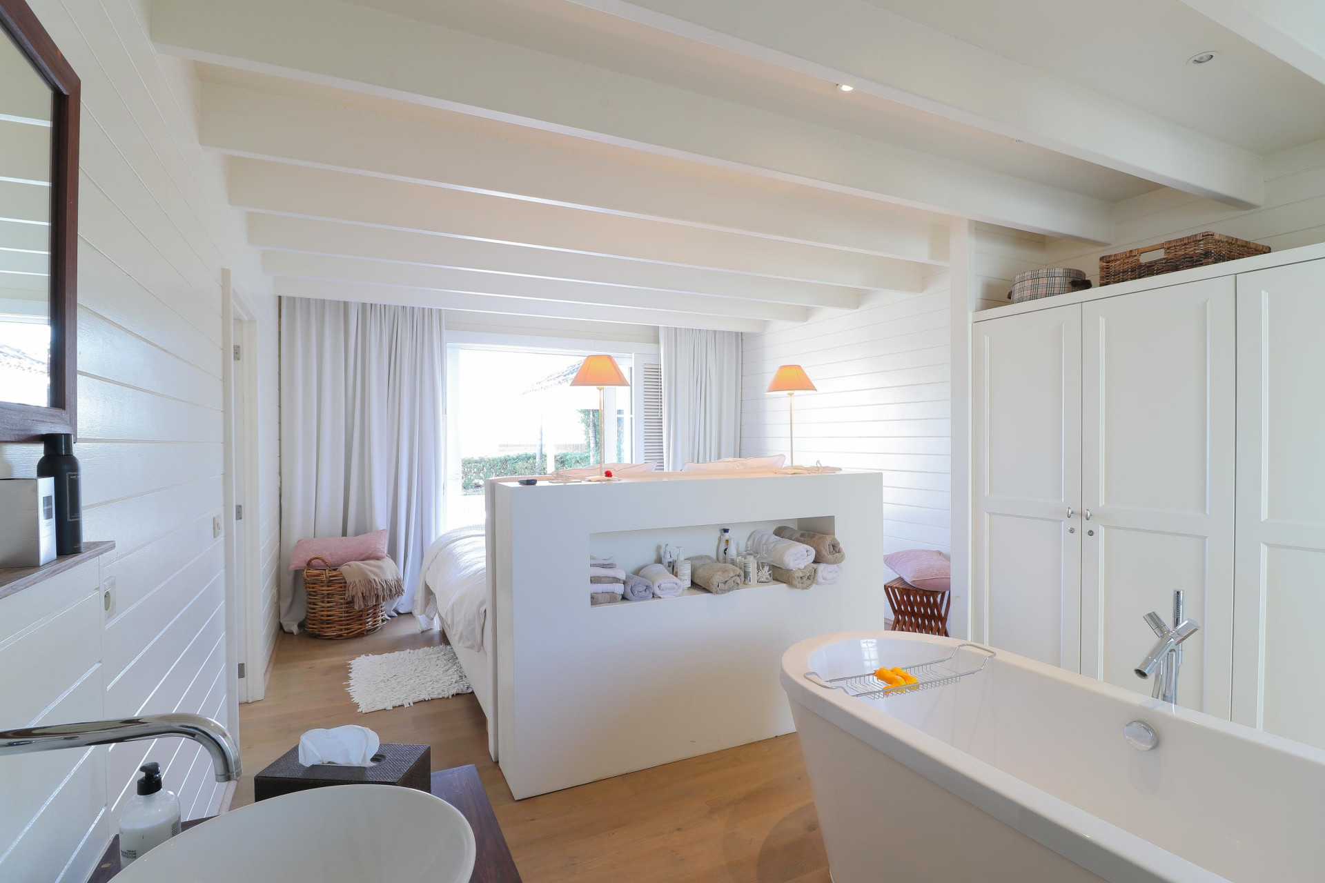 Bedroom with a partial wall divider, separating the sleeping area from a freestanding bathtub and sink.