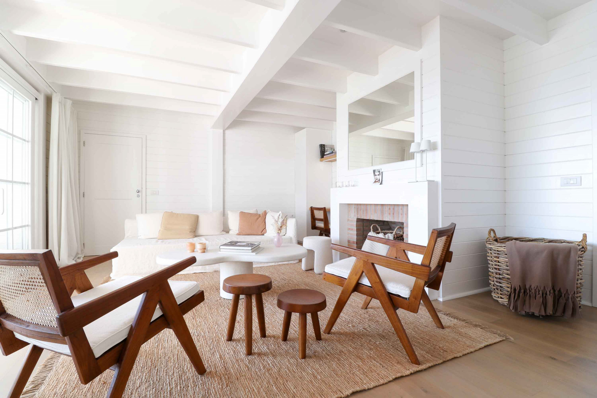 Living room with white walls and ceiling beams, light sofa, two wooden chairs, and fireplace.