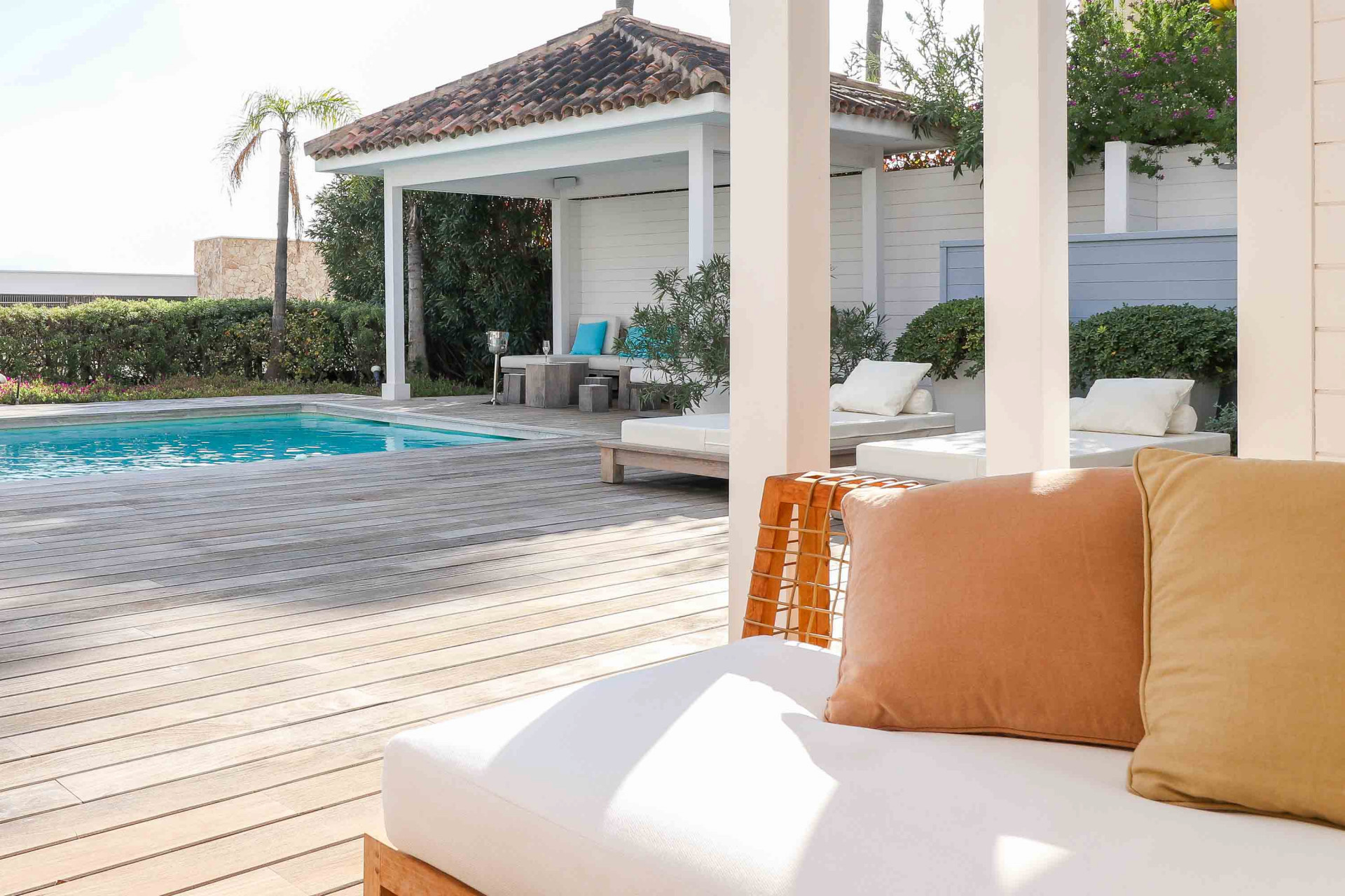 Low angle view of a wooden deck and pool, with a shaded seating area in the background.