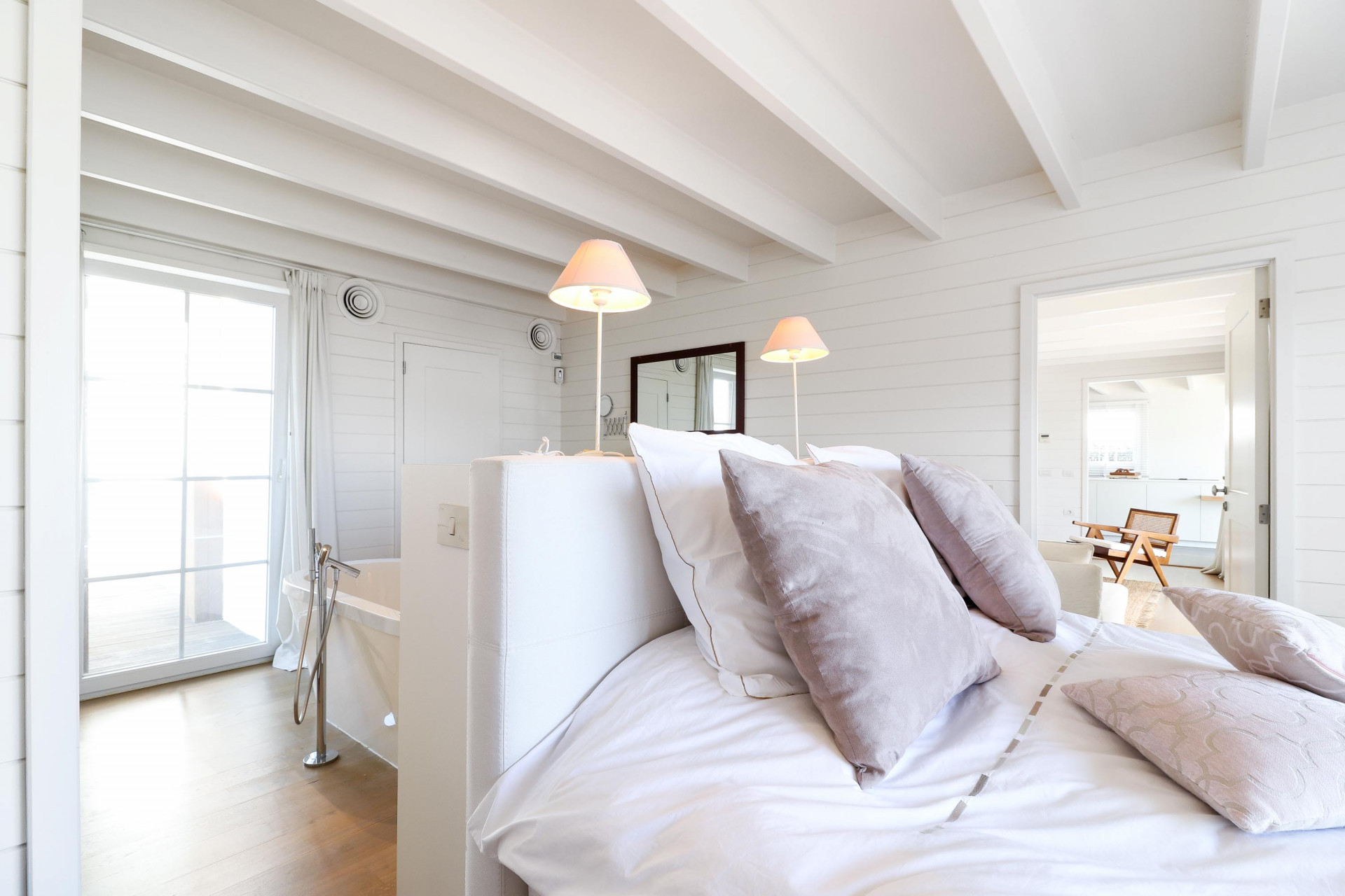 Bedroom view towards glass doors to a deck, showing a freestanding tub and two bedside lamps.