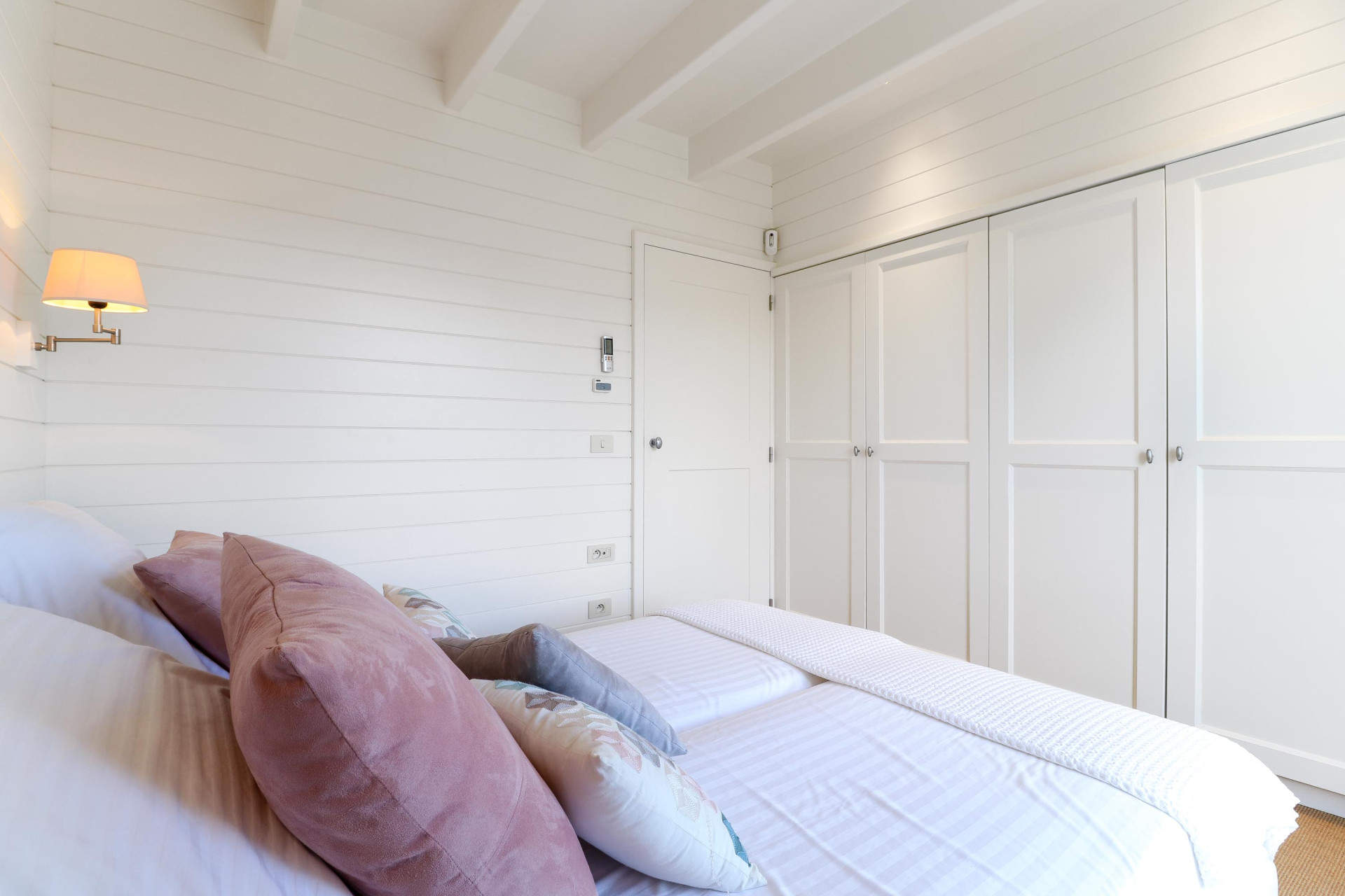 Bedroom with white shiplap walls, twin beds with pink and gray pillows, and built-in white wardrobes.