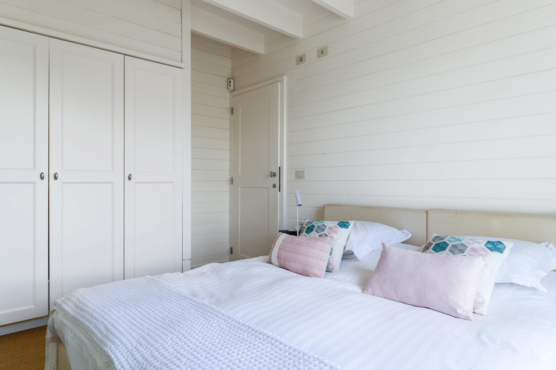 Bedroom featuring white plank walls, built-in wardrobes, a closed door, and a bed with light bedding.