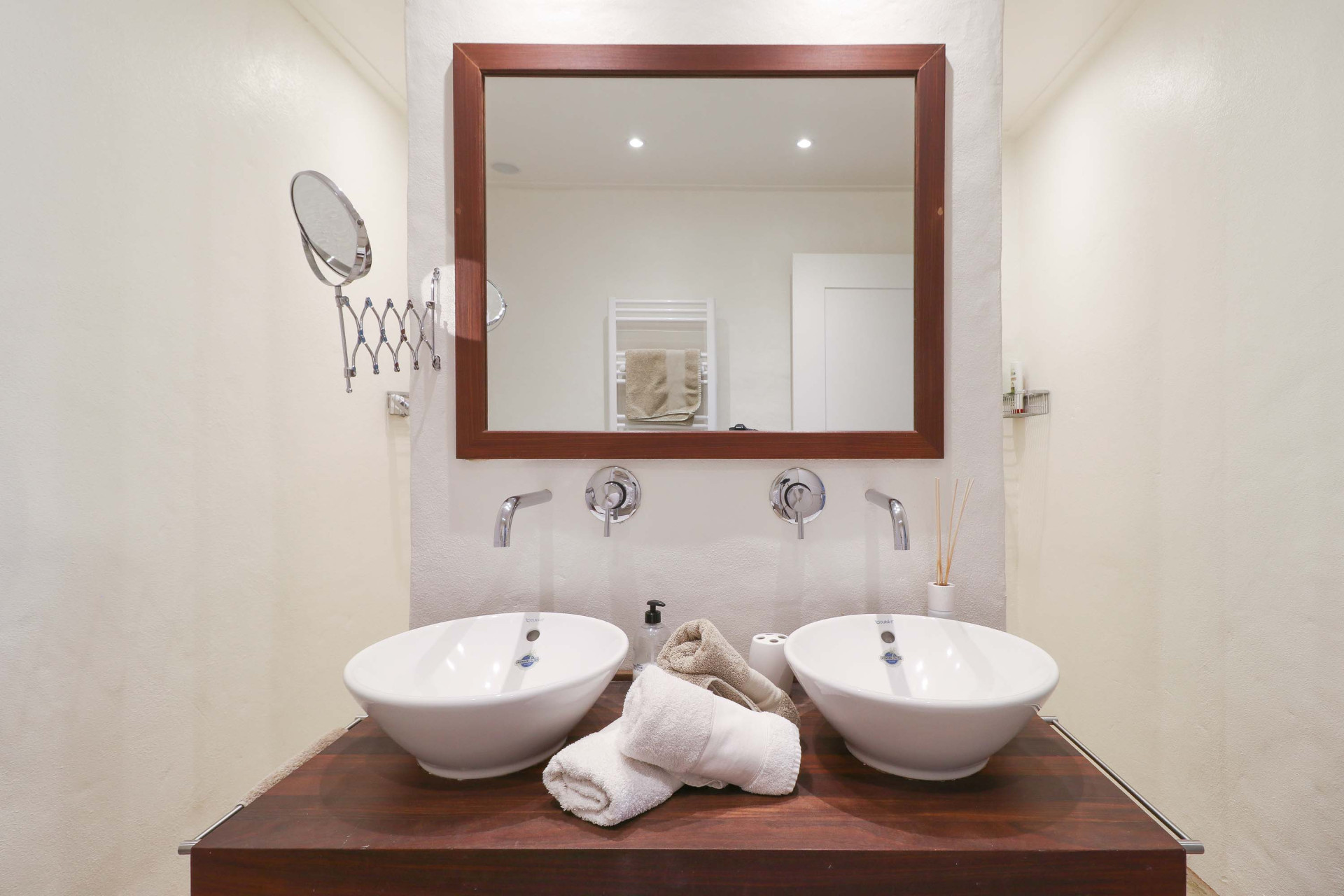 Close-up of a bathroom vanity with two white vessel sinks, chrome faucets, and a framed mirror above.