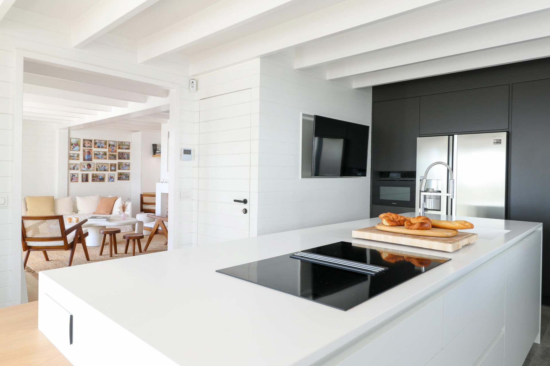 Kitchen with white island and black wall cabinetry, looking into an open plan living area beyond.