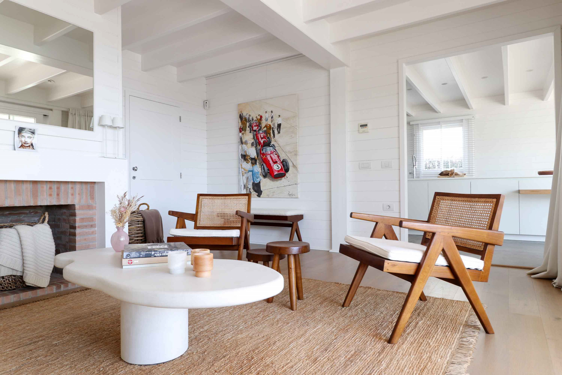 Living room with two wooden chairs, coffee table, and an artwork of race cars visible through doorway.