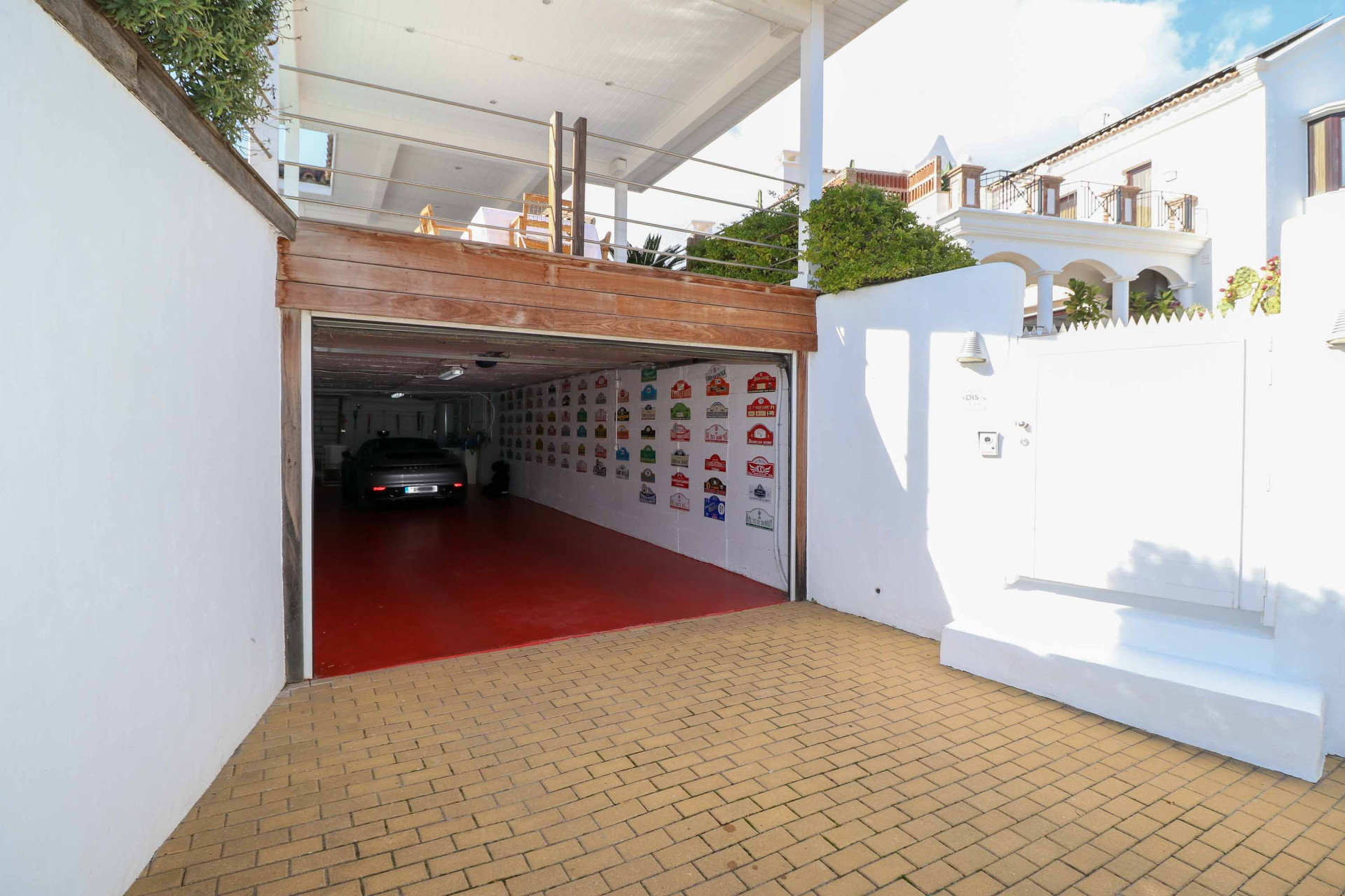 Open garage entrance with a red floor, a silver car inside, and a tiled driveway.