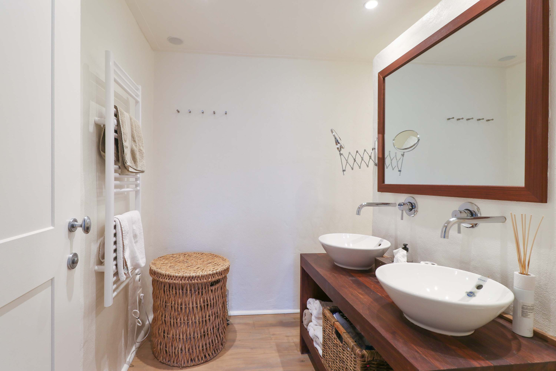 Bathroom with dual white vessel sinks on a wooden vanity, a large framed mirror, and a towel warmer rack.