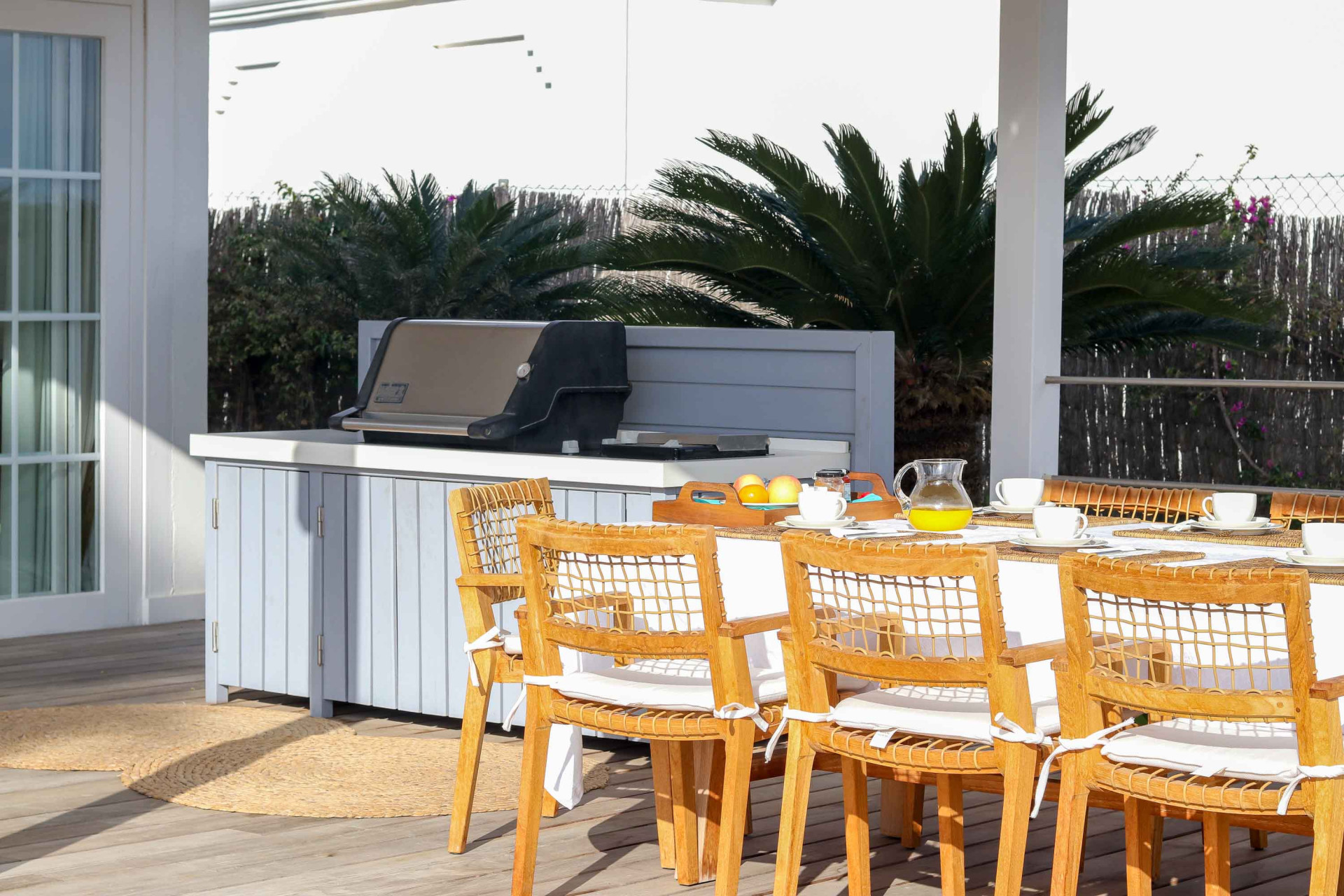 Outdoor dining area with a long table and a grill station on a wooden deck.