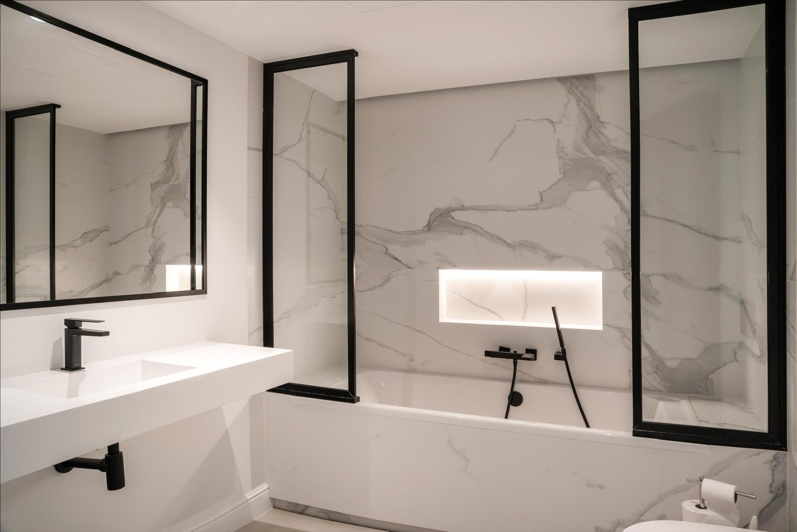 Contemporary bathroom featuring a bathtub, dual mirrors, and marble walls.
