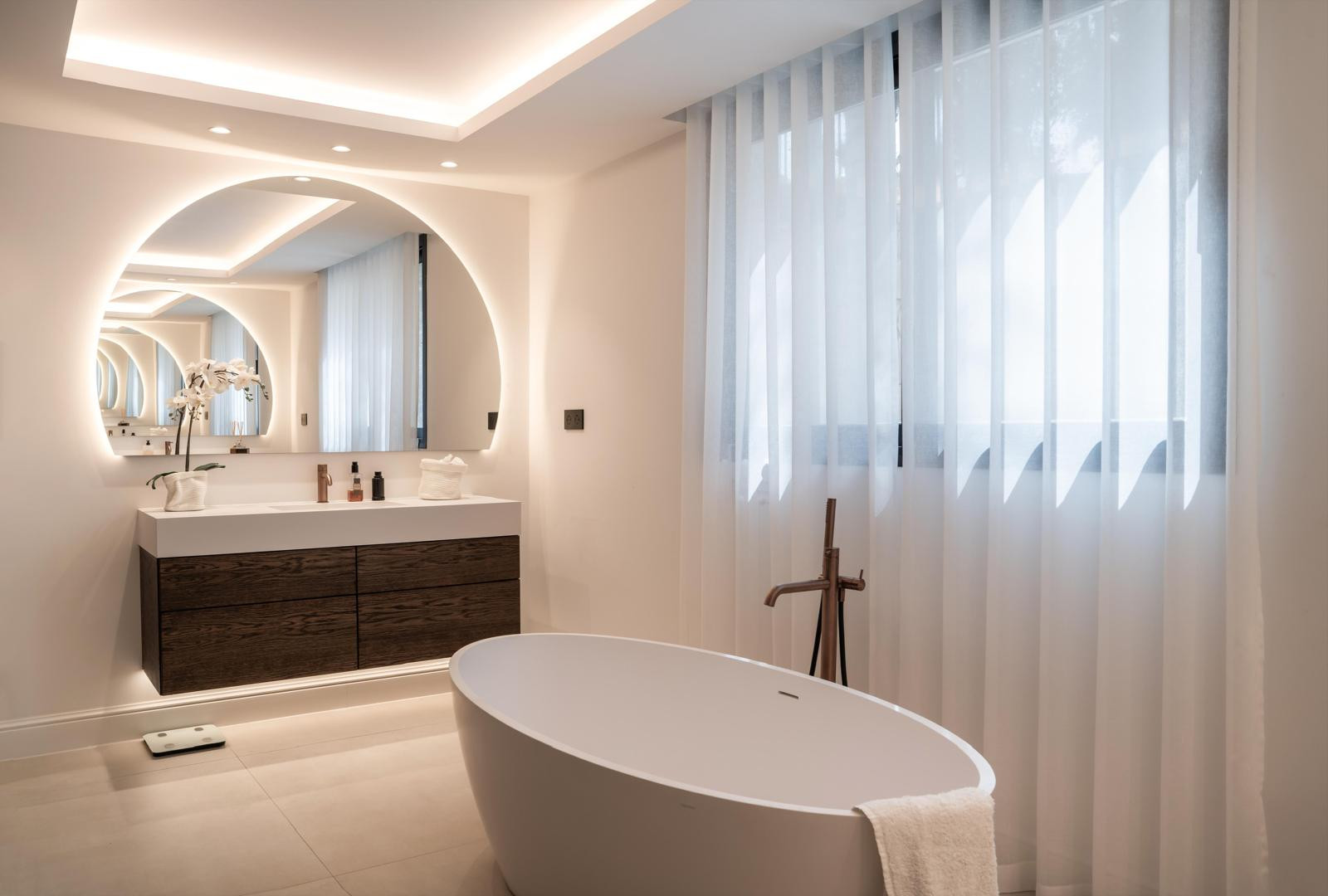 Elegant bathroom with a freestanding tub and a large, round mirror above the sink.