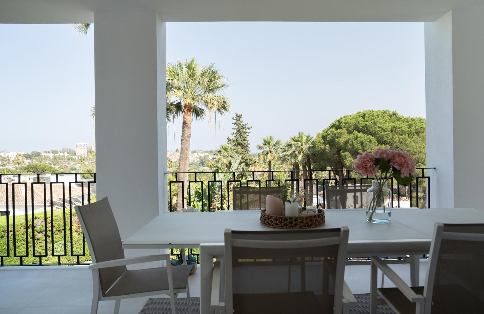 View from the terrace showcasing a dining setup and surrounding greenery and palm trees.