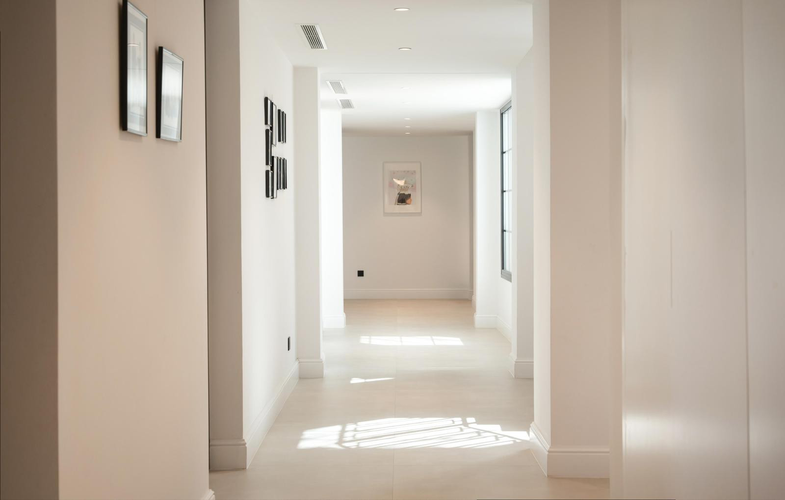 Long hallway illuminated by natural light, adorned with framed pictures on the walls.