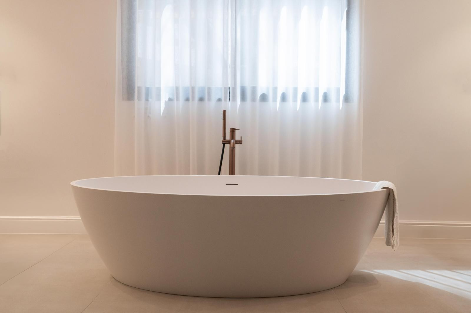 Close-up of the white bathtub with a towel draped over and sheer curtains in the background.