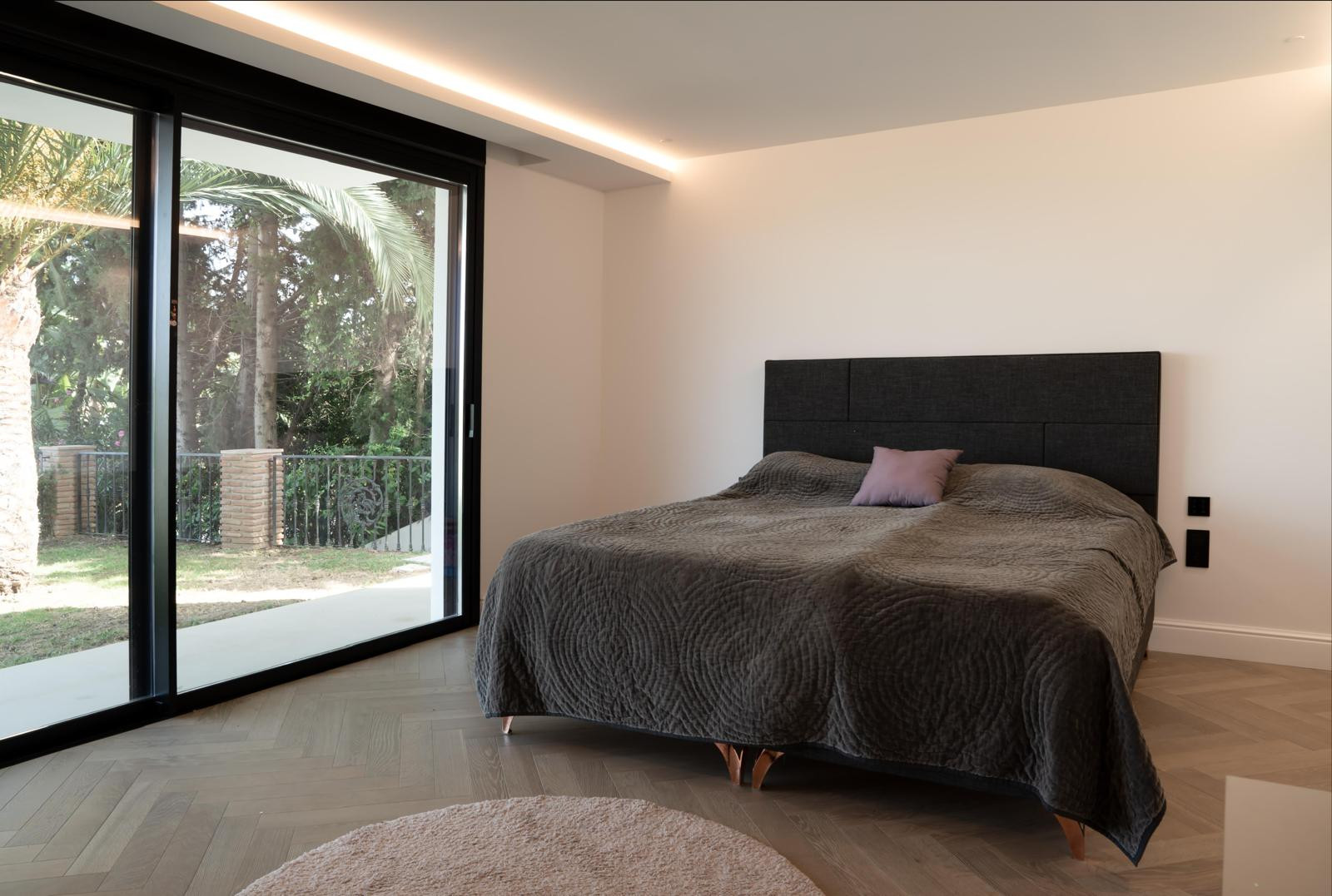 Bedroom view with a bed, natural light, and greenery outside.