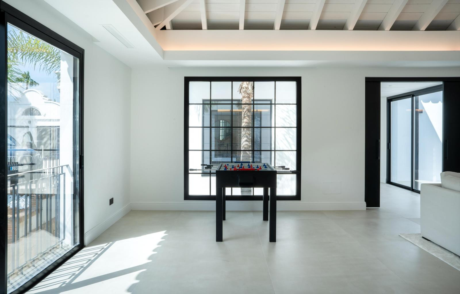 Bright room with a foosball table and large windows overlooking palm trees.