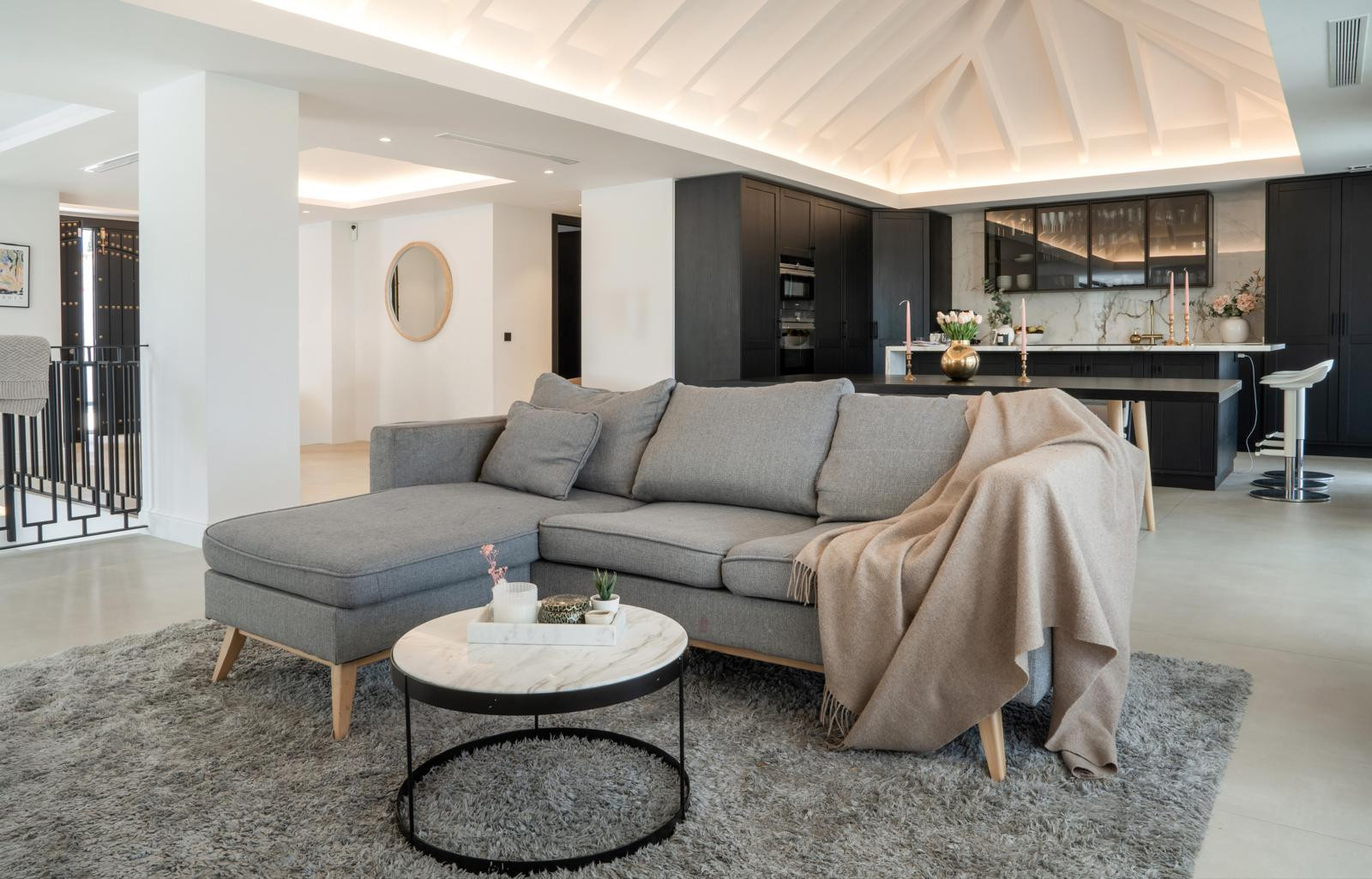 Living room with a gray sectional sofa, round coffee table and a view of the kitchen area.