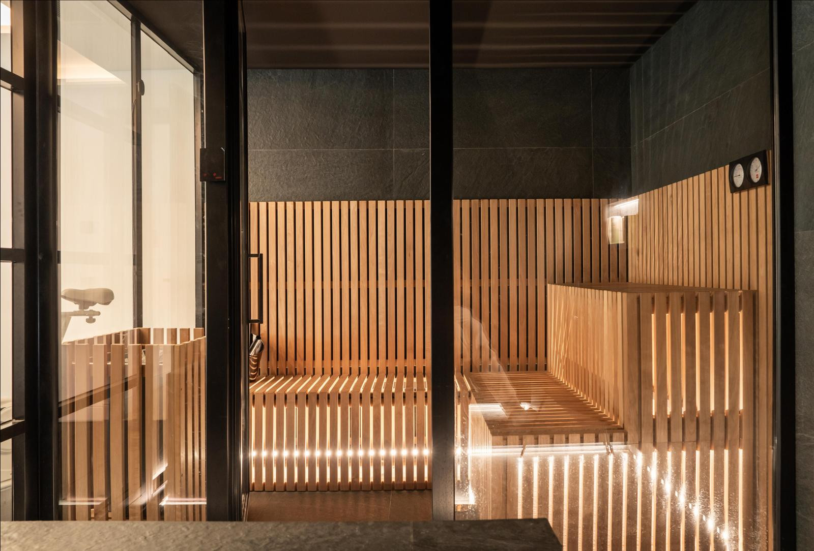 Sauna area with wooden benches and ambient lighting, visible through glass panels.