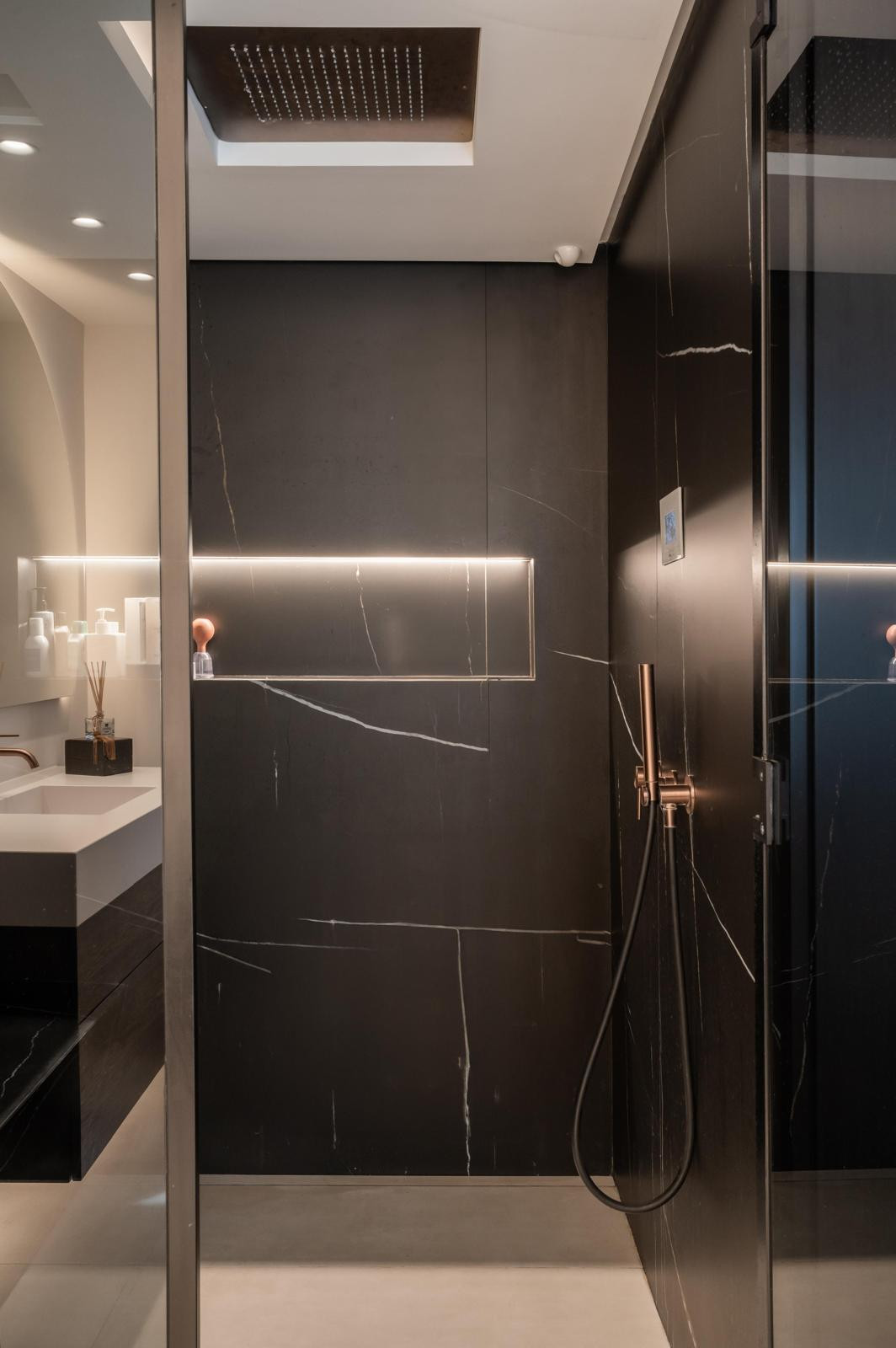Modern shower with dark walls, rainfall shower head, and illuminated niche.
