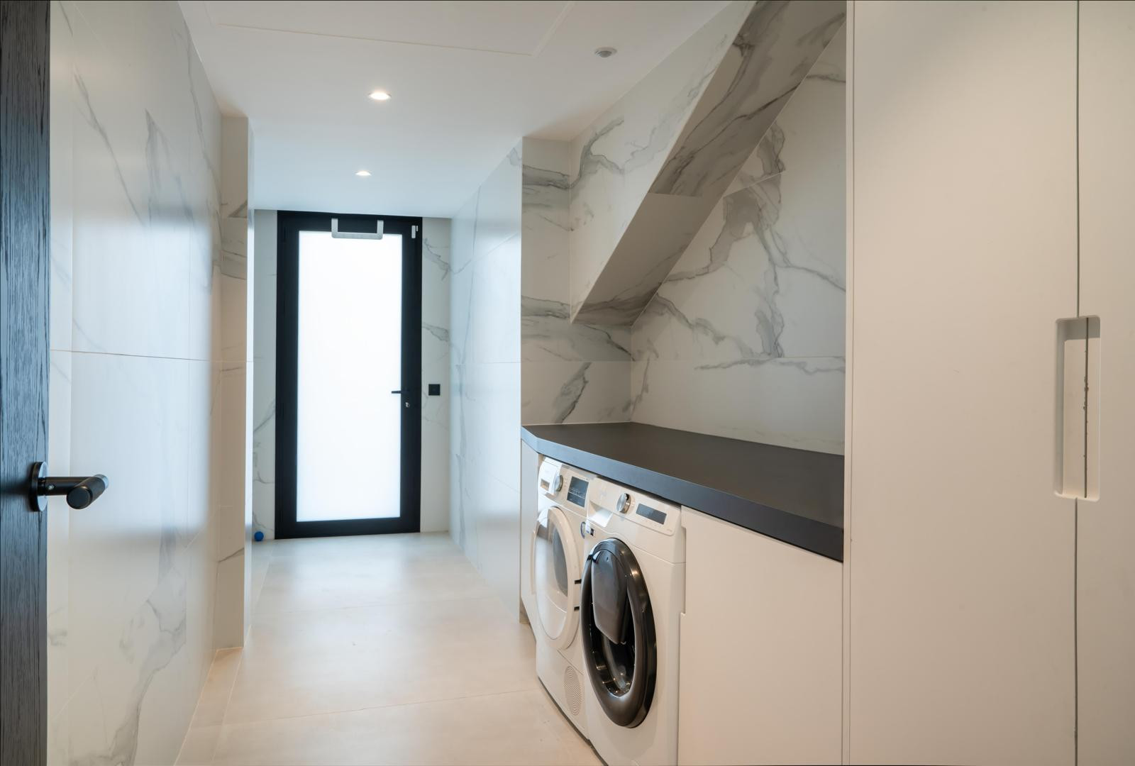 Laundry room with marble walls, washing machines, and a glass door leading outside.