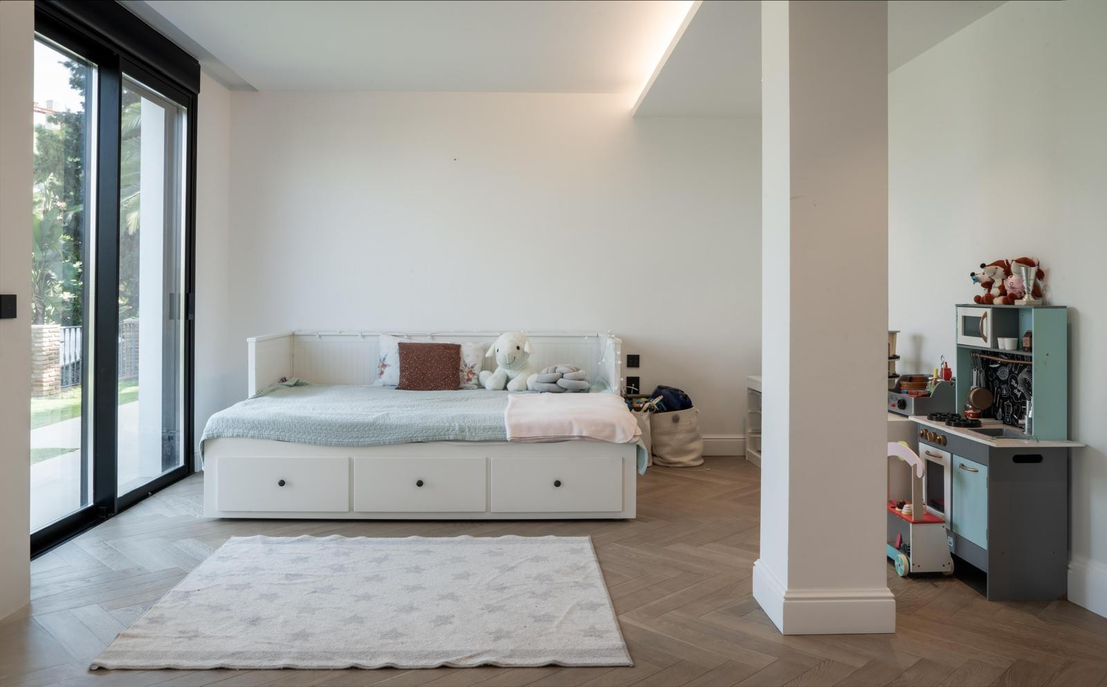 Children's room with a daybed, toys, and large windows overlooking the garden.