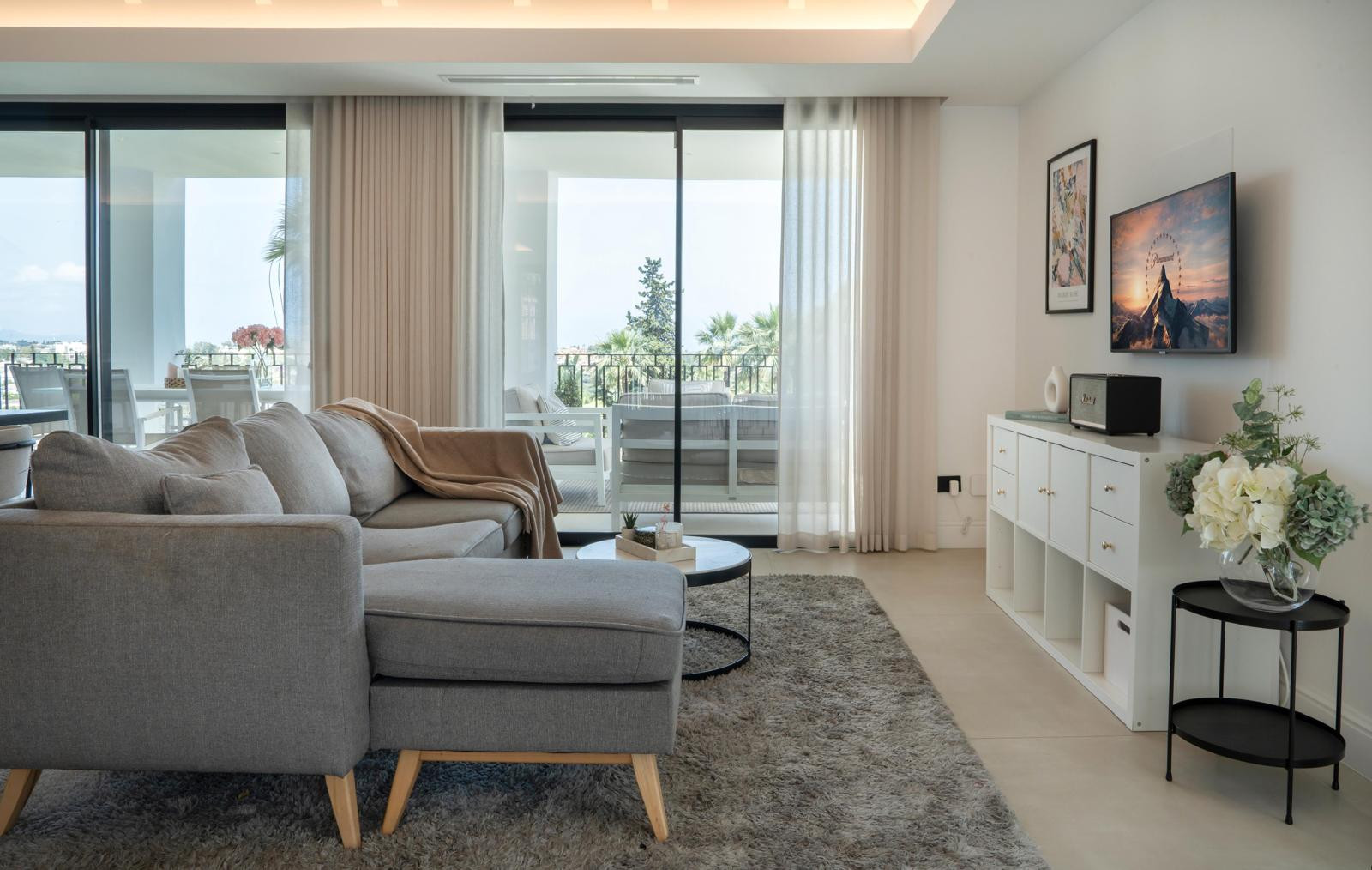 Cozy living room with a gray sofa, large windows, and a TV mounted on the wall.