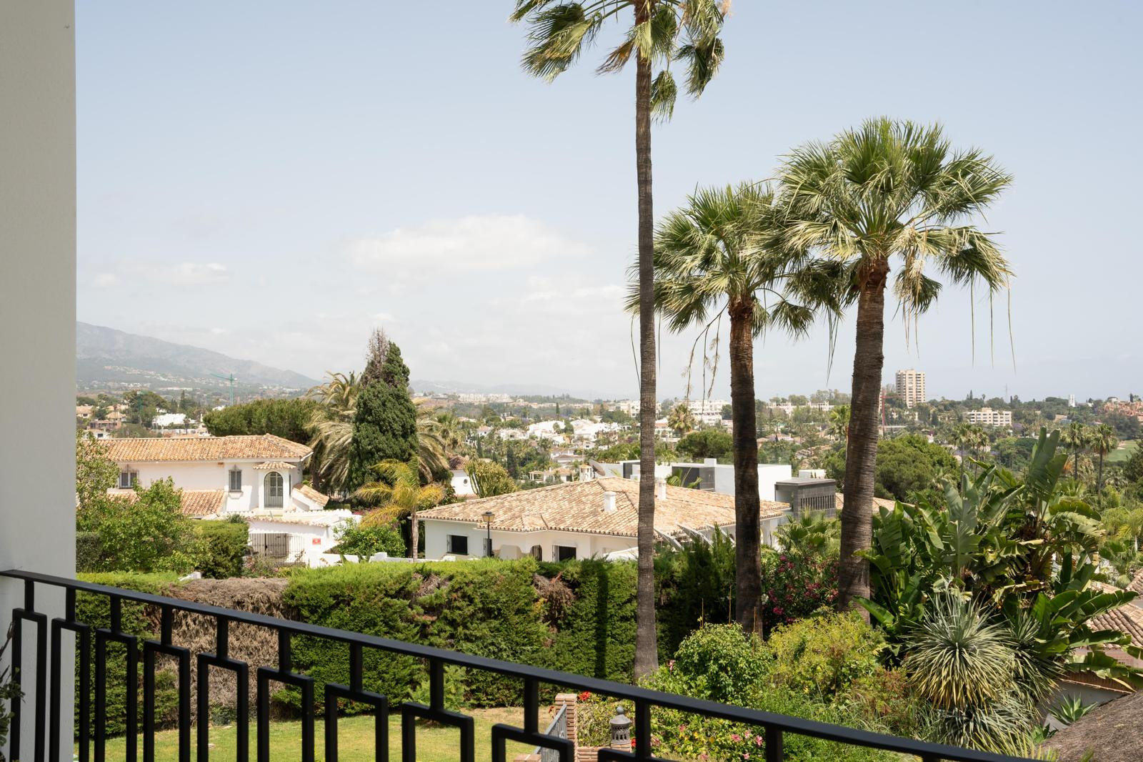 View from balcony showing palm trees and nearby villas against a backdrop of mountains and blue sky.