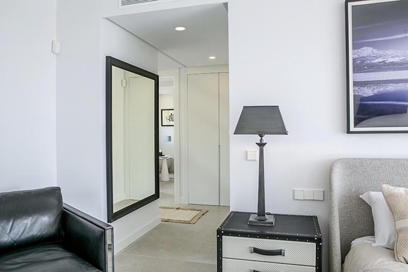 Bedroom view showing a bed, black leather chair, and a hallway with a large mirror.