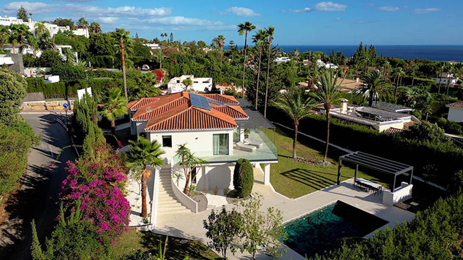 Aerial view of the villa with a red tile roof, pool, terraced gardens, and ocean in the background.