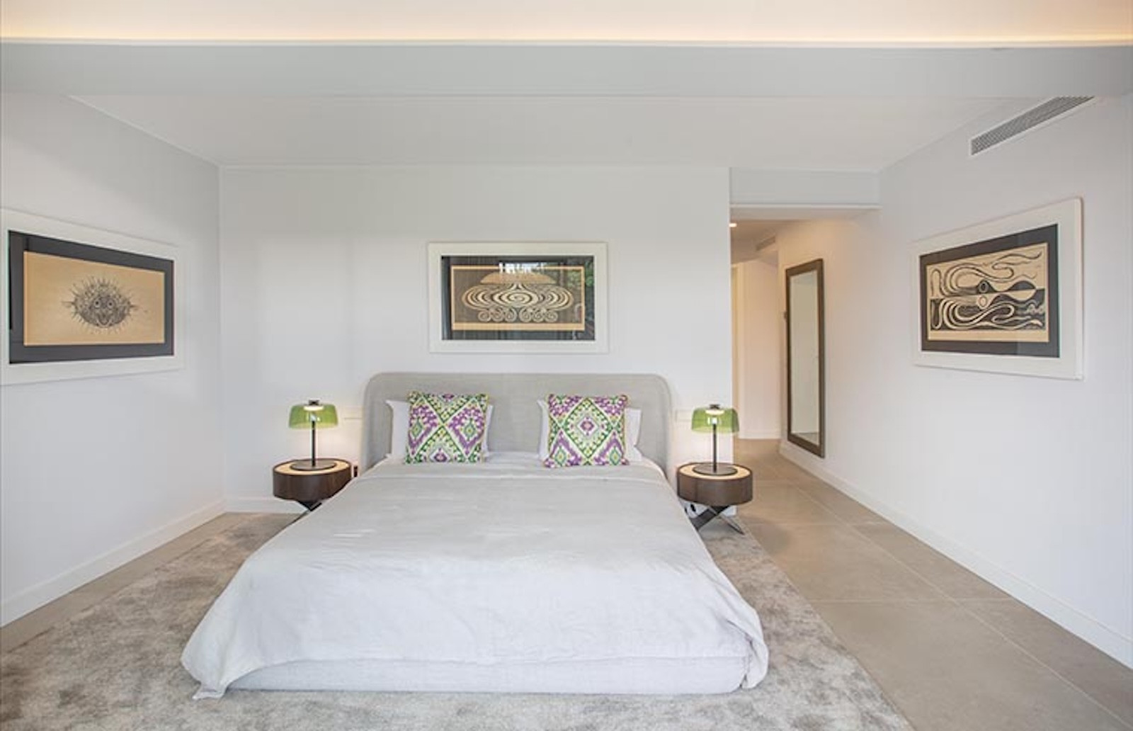 Bedroom with a large bed, two nightstands with green lamps, and three abstract artworks.