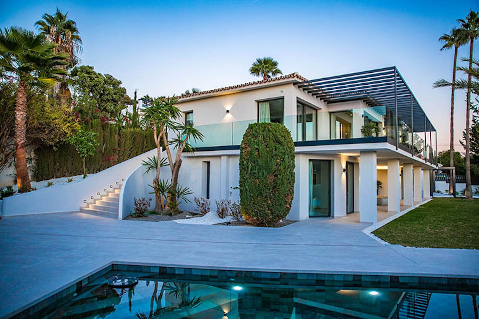 Exterior view of a modern white villa with multiple balconies, a swimming pool, and curved staircase.