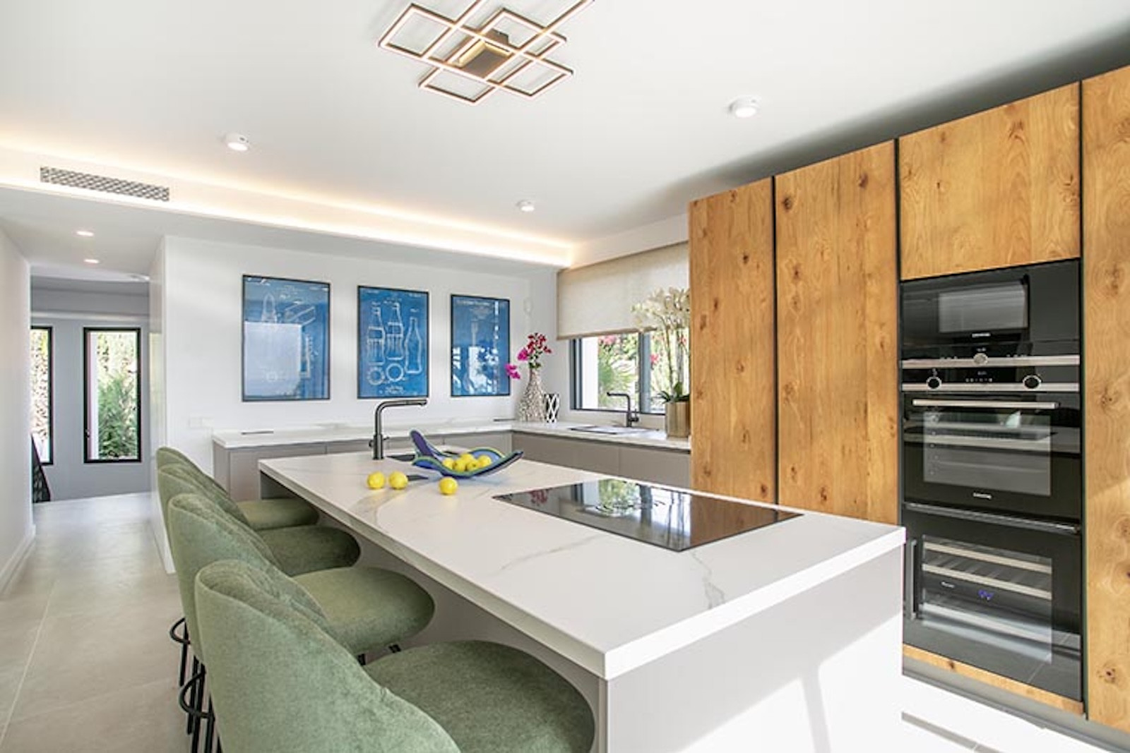 Kitchen with wooden cabinetry, integrated appliances, a large white island with a stovetop, and green chairs.