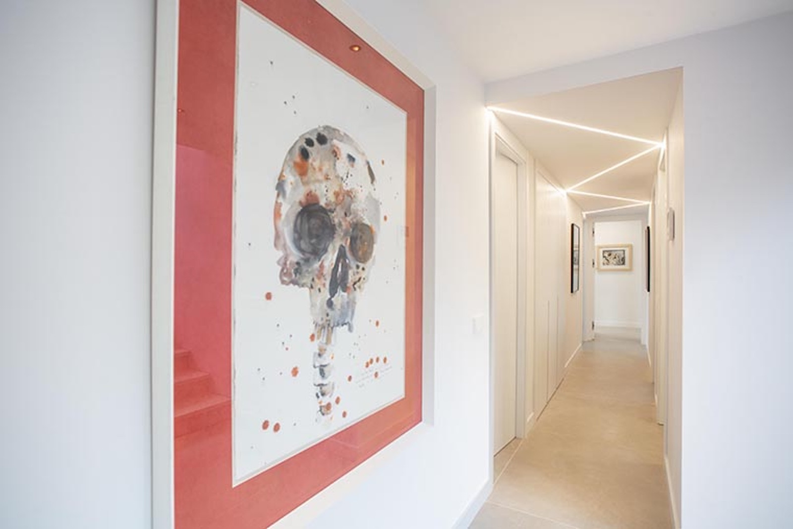 White hallway with linear LED lighting on the ceiling, a framed skull artwork, and closed doors.
