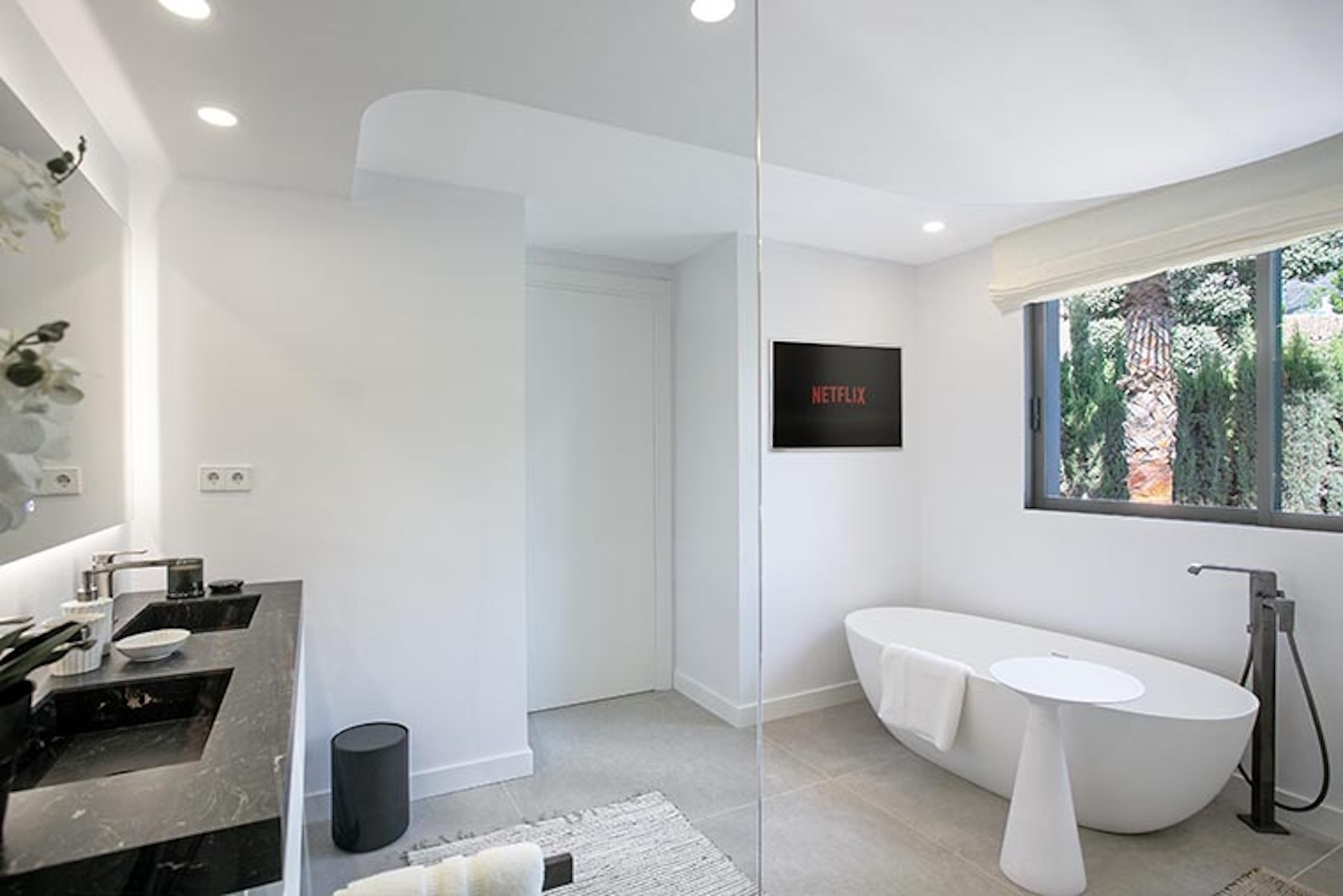 Bathroom with a large white freestanding tub, dual vanity, and a wall-mounted TV.