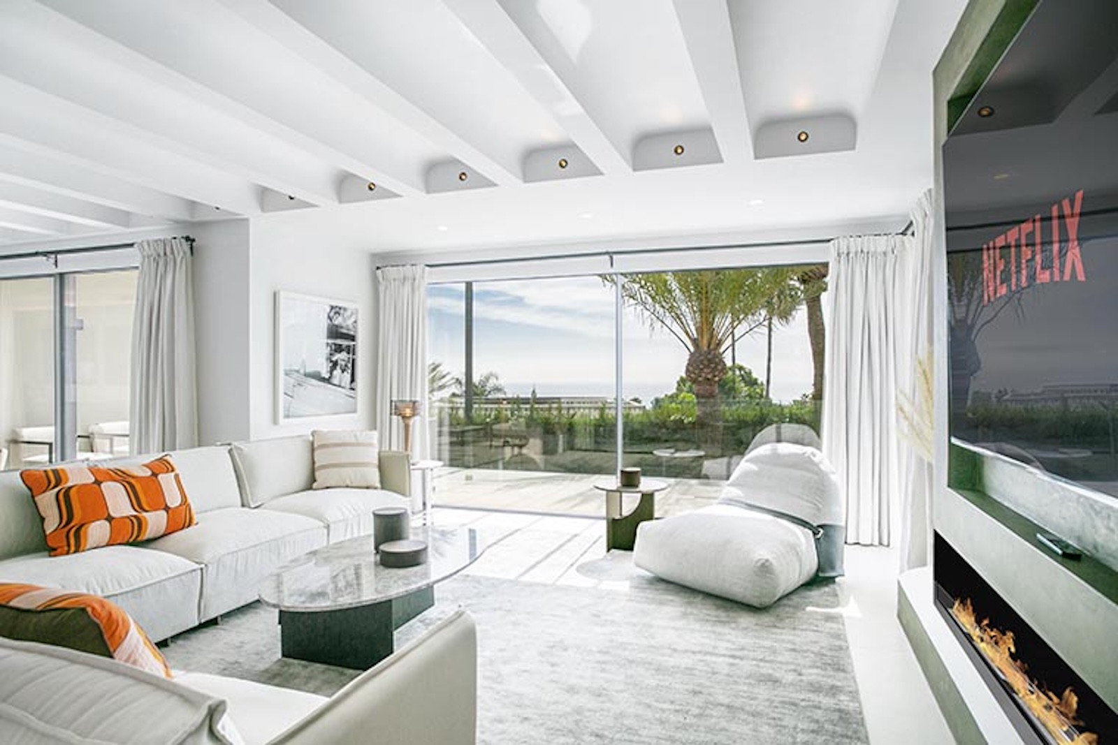 Living room with white sofas facing a wall-mounted TV and large glass doors opening to an outdoor view.