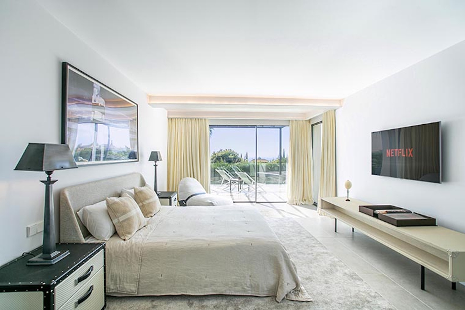 Bright bedroom with a large bed, two side tables, a wall-mounted TV, and sliding doors to an outdoor patio.