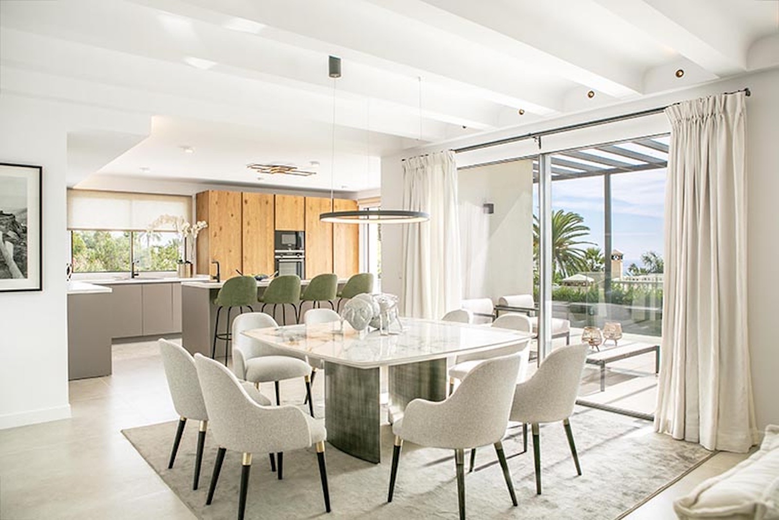 Dining area with marble table and upholstered chairs, next to large glass doors leading outdoors.