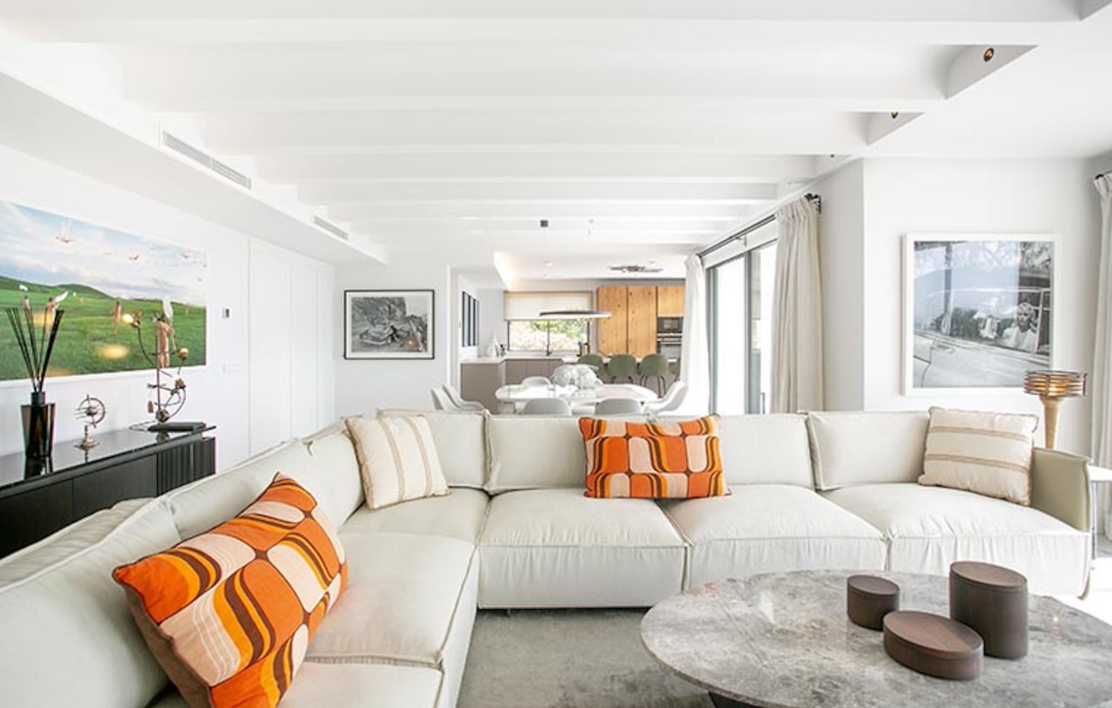 White living room with large sectional sofa, orange pillows, and abstract art on the wall.