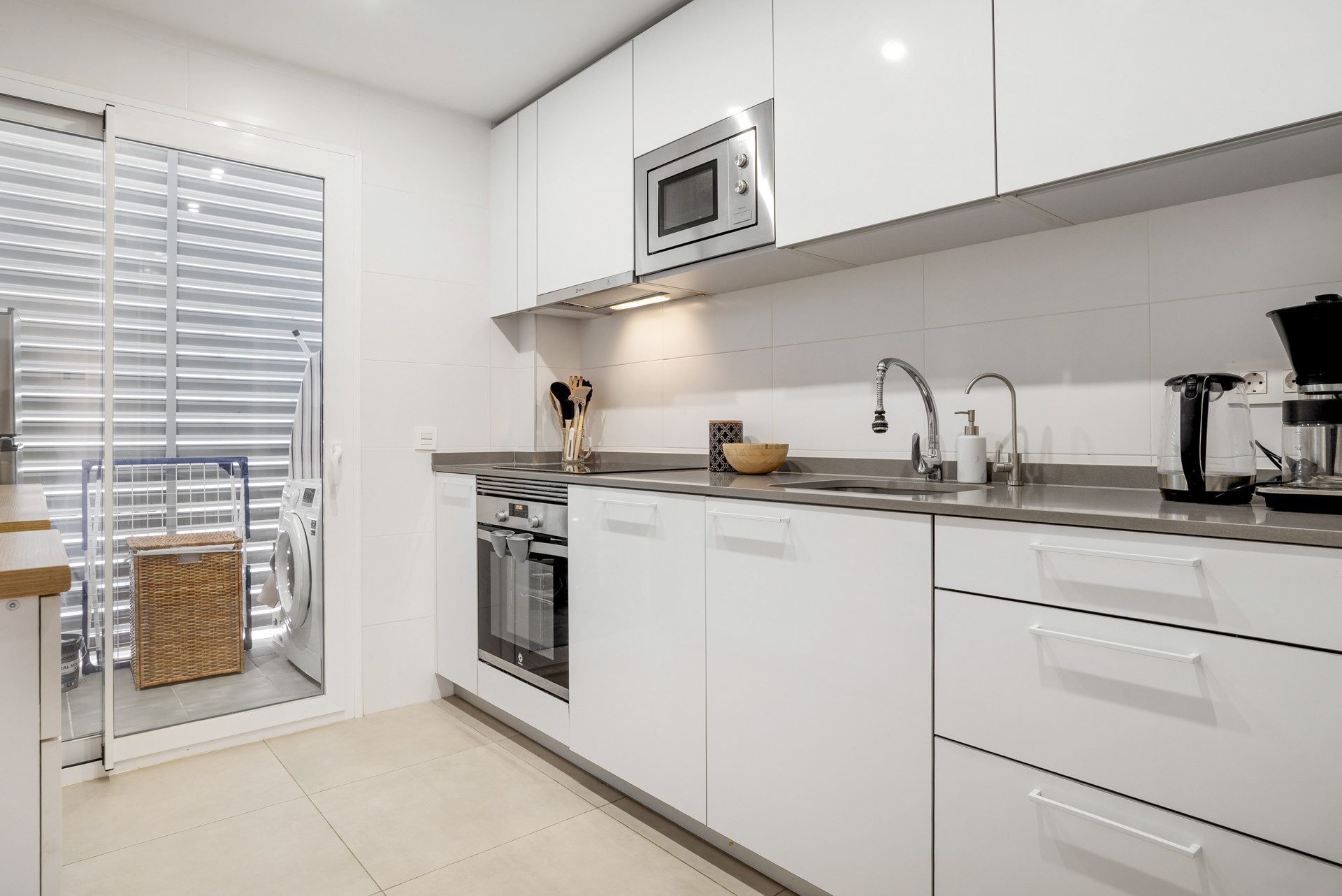 Bright kitchen with white cabinets, stainless steel sink, microwave, oven, and balcony access.