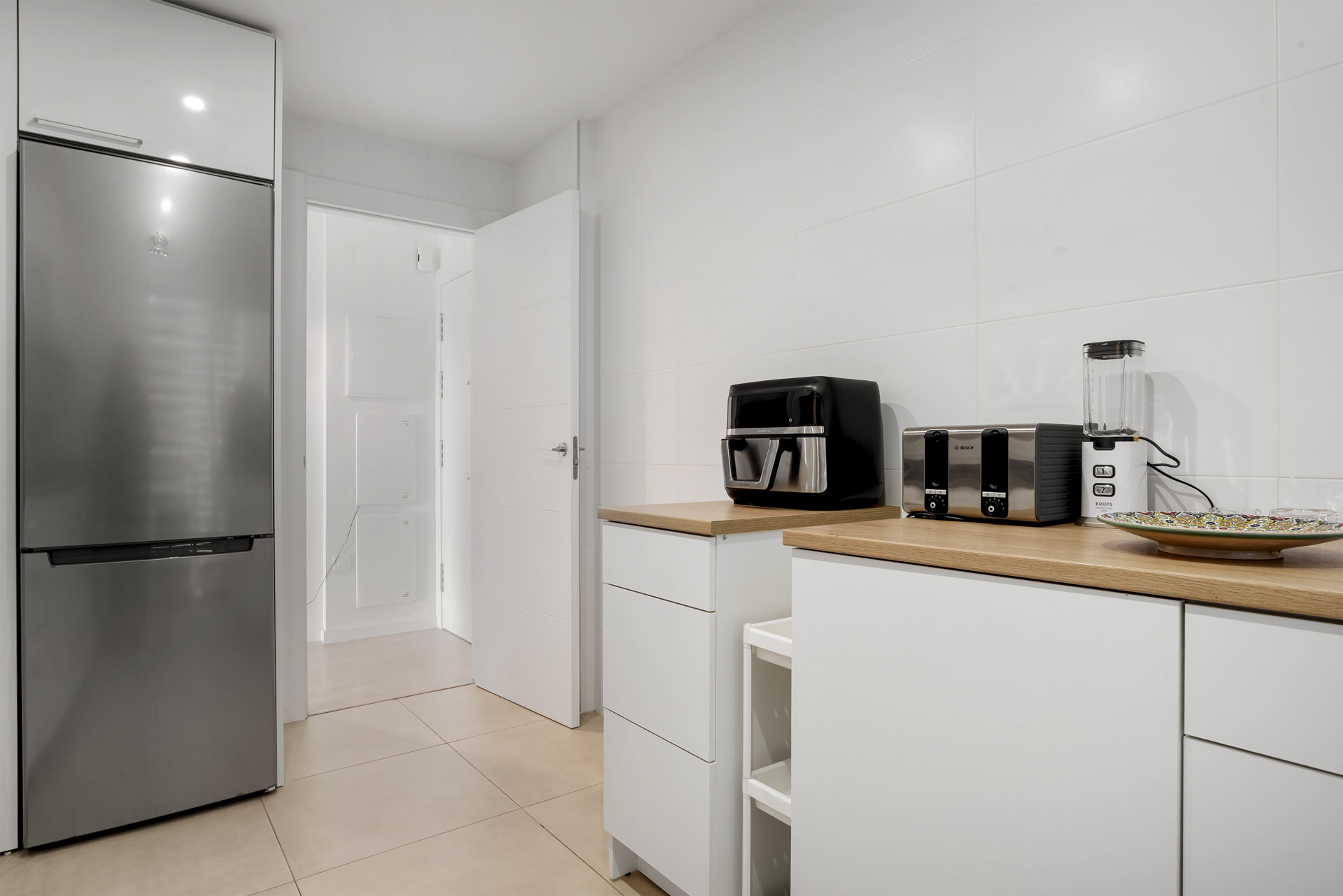 Kitchen view with a stainless steel refrigerator, white tile walls, and a wood countertop with appliances.