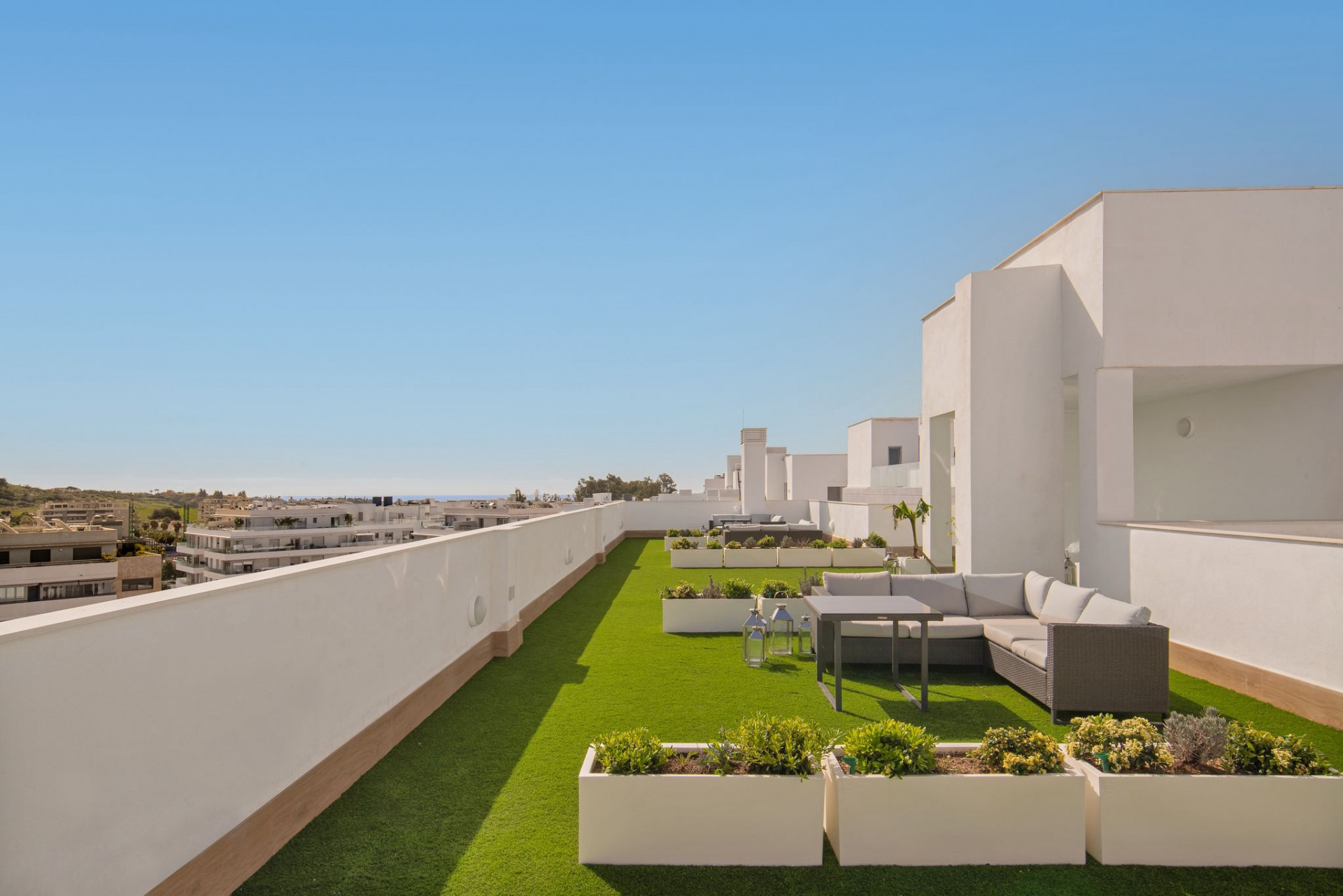 Rooftop terrace with artificial grass, a grey sectional sofa, coffee table, and white planters.