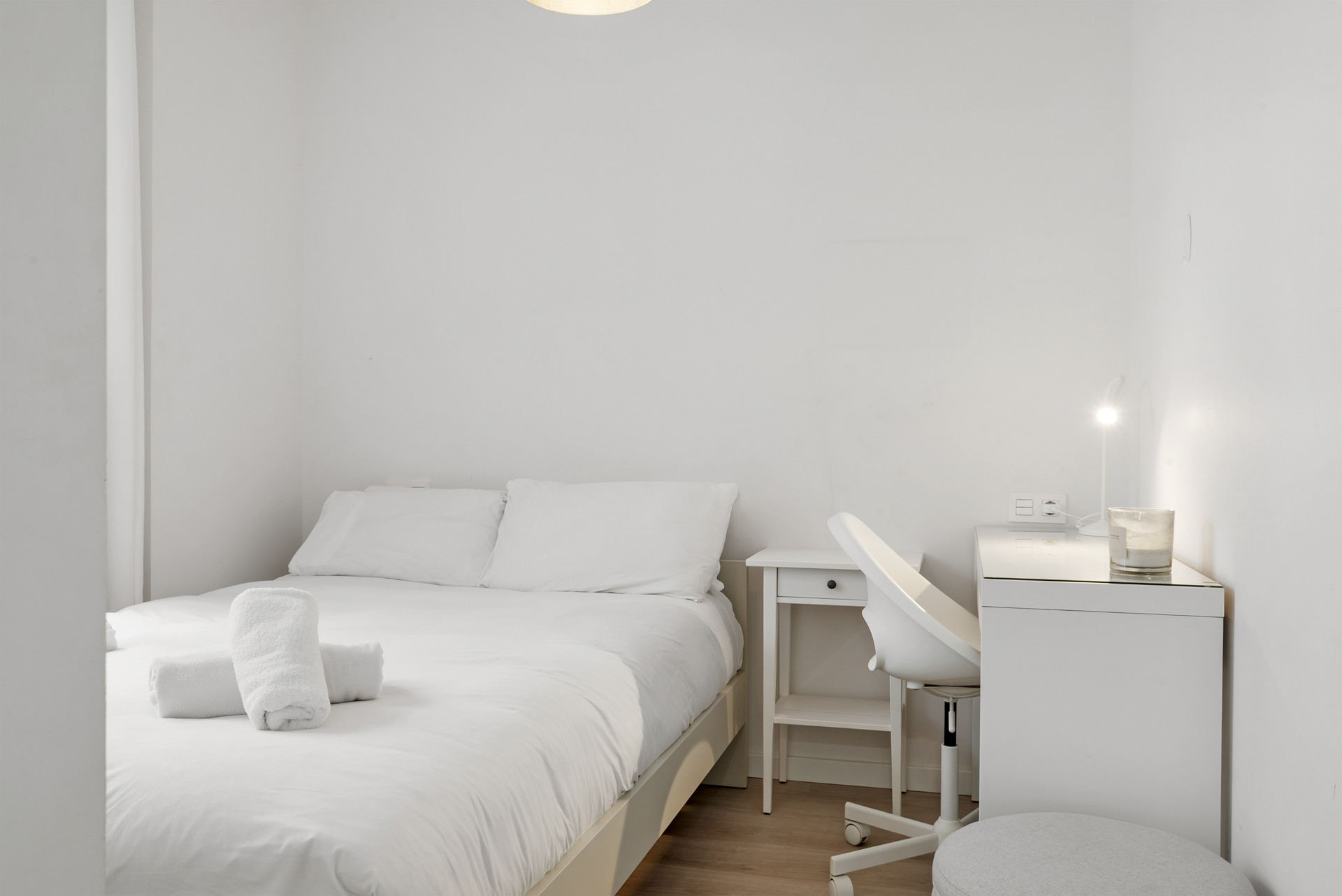 Small white bedroom with a bed, white nightstand, white desk, and a white office chair.