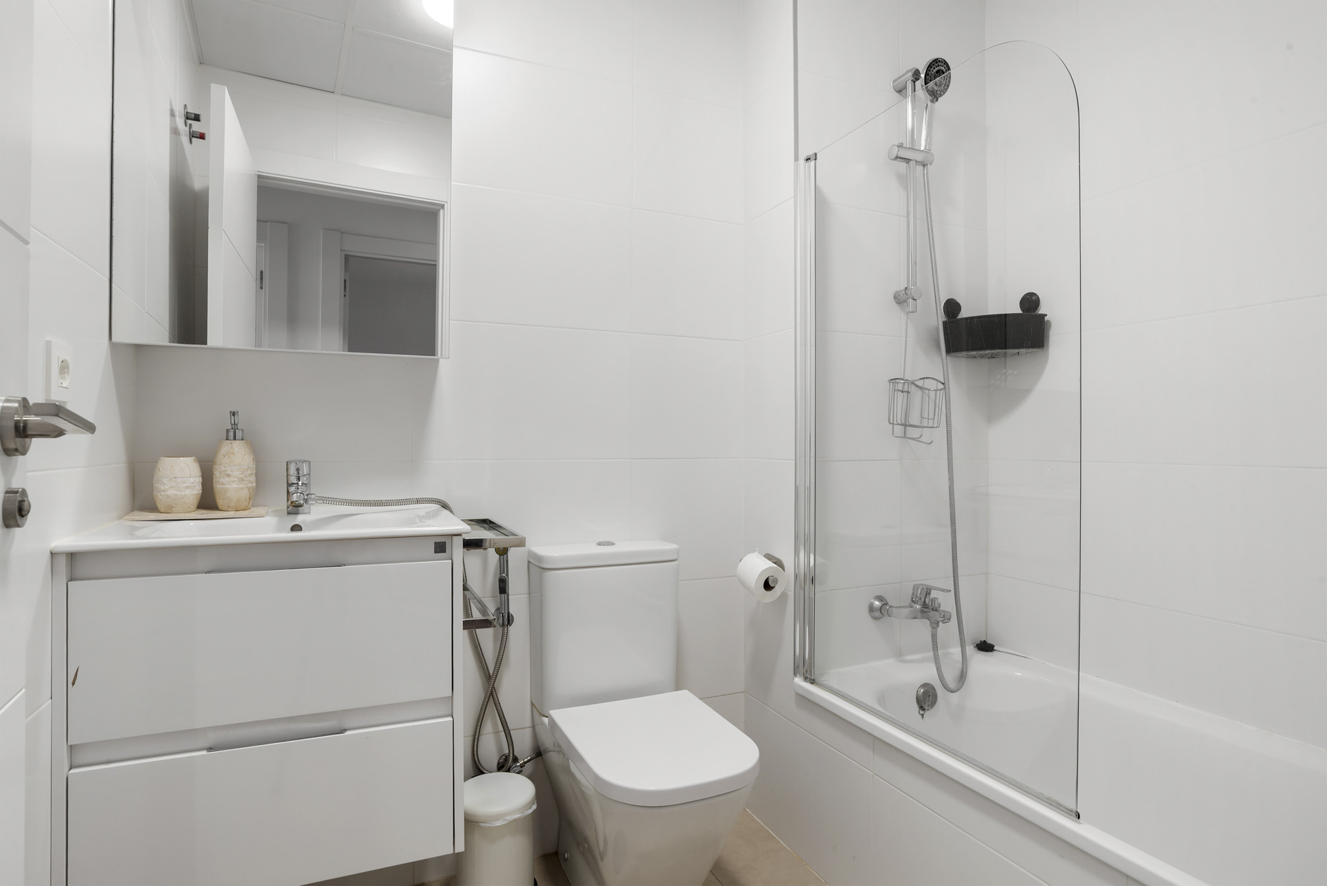 Bathroom with a white vanity, toilet, and a bathtub with a glass shower screen and white tiled walls.