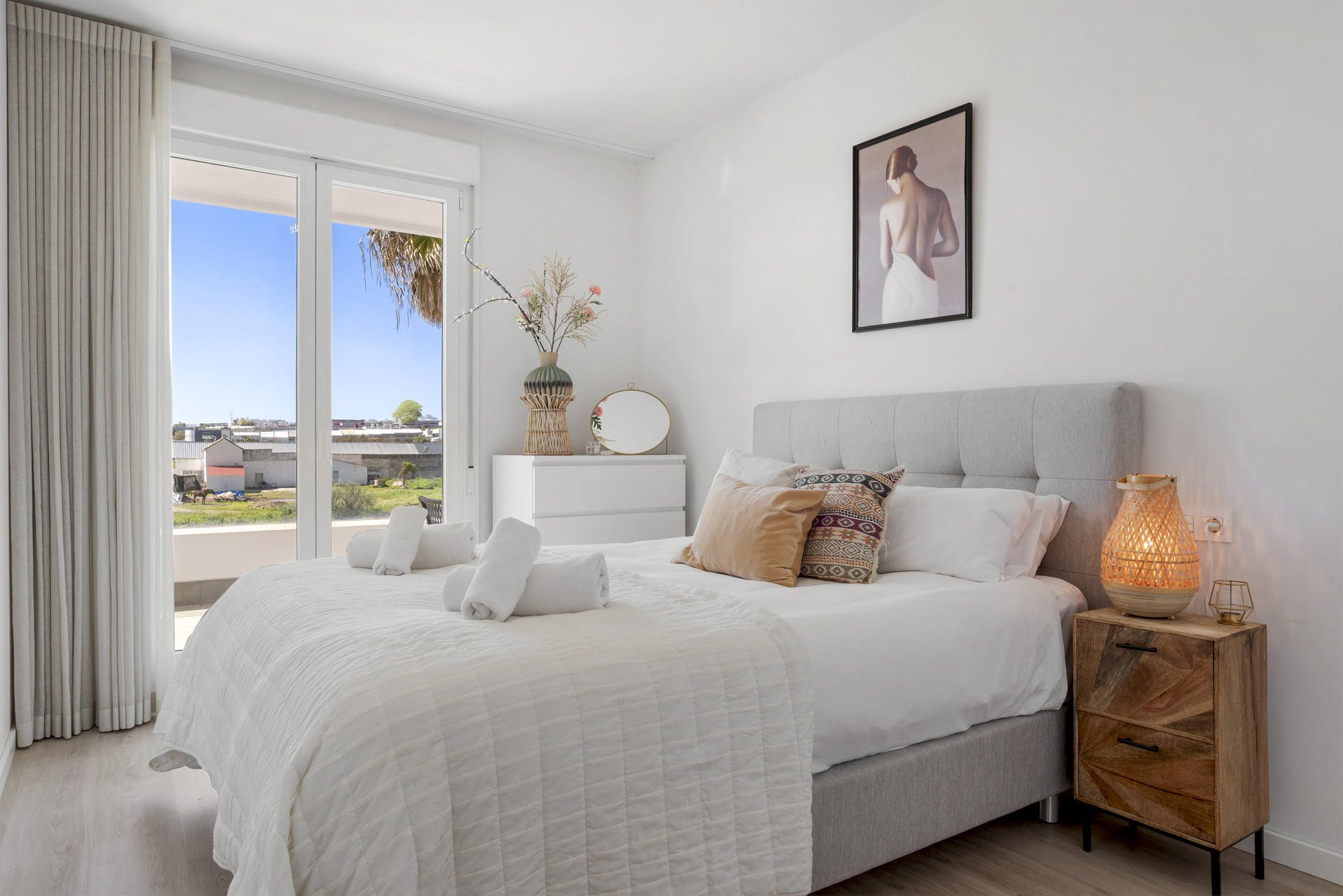 Bedroom with white bedding, a gray headboard, and sliding glass doors opening to a balcony view.